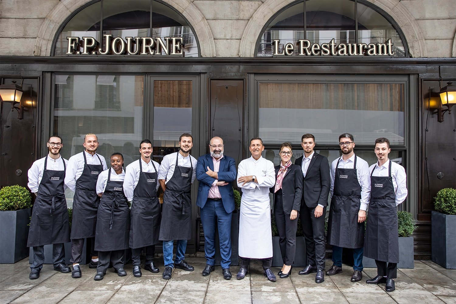 Group of people in front of "F.P. Journe Le Restaurant", wearing work uniforms.