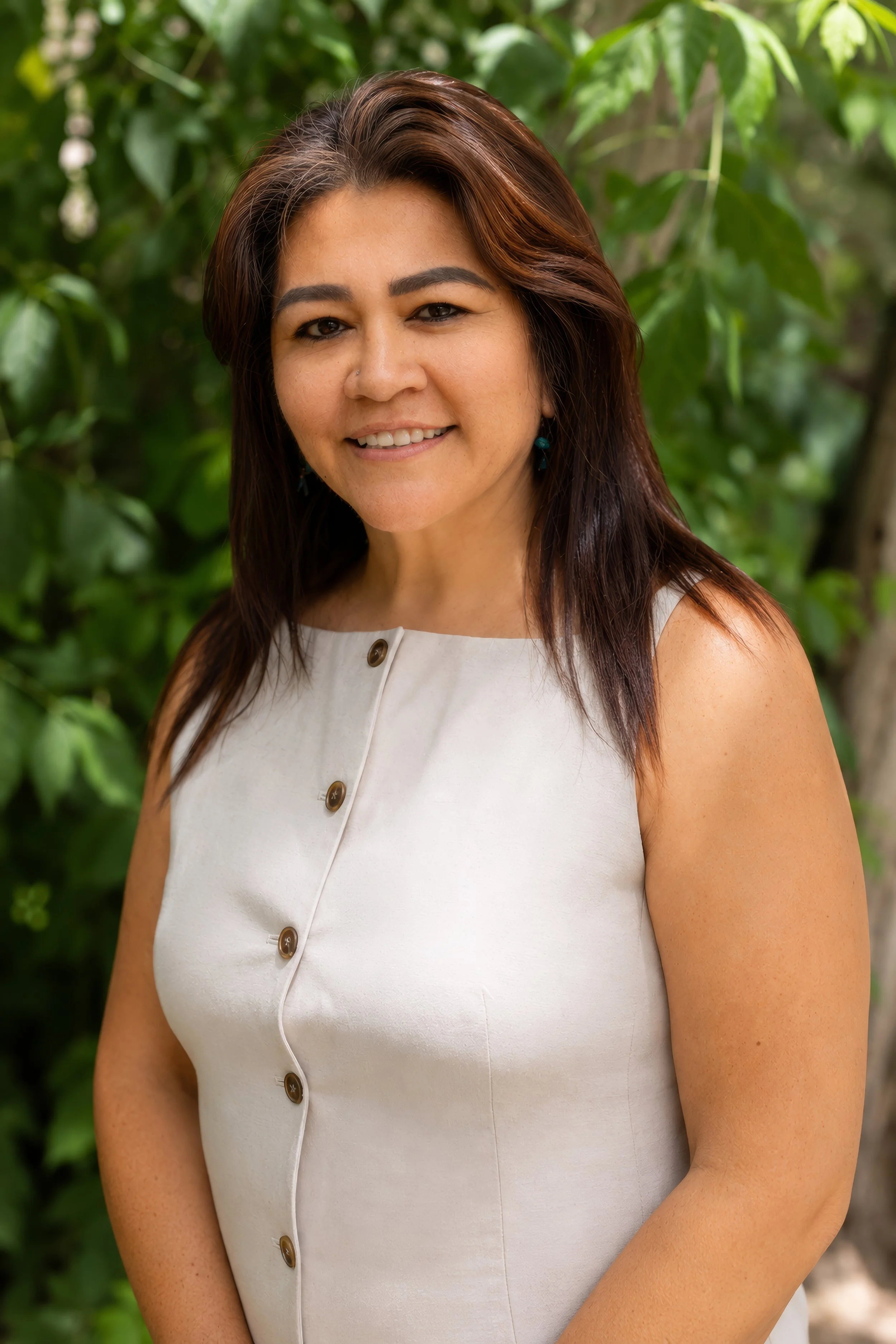 A woman smiling outdoors in front of a teal wooden wall, wearing a dark shirt and a purple vest.
