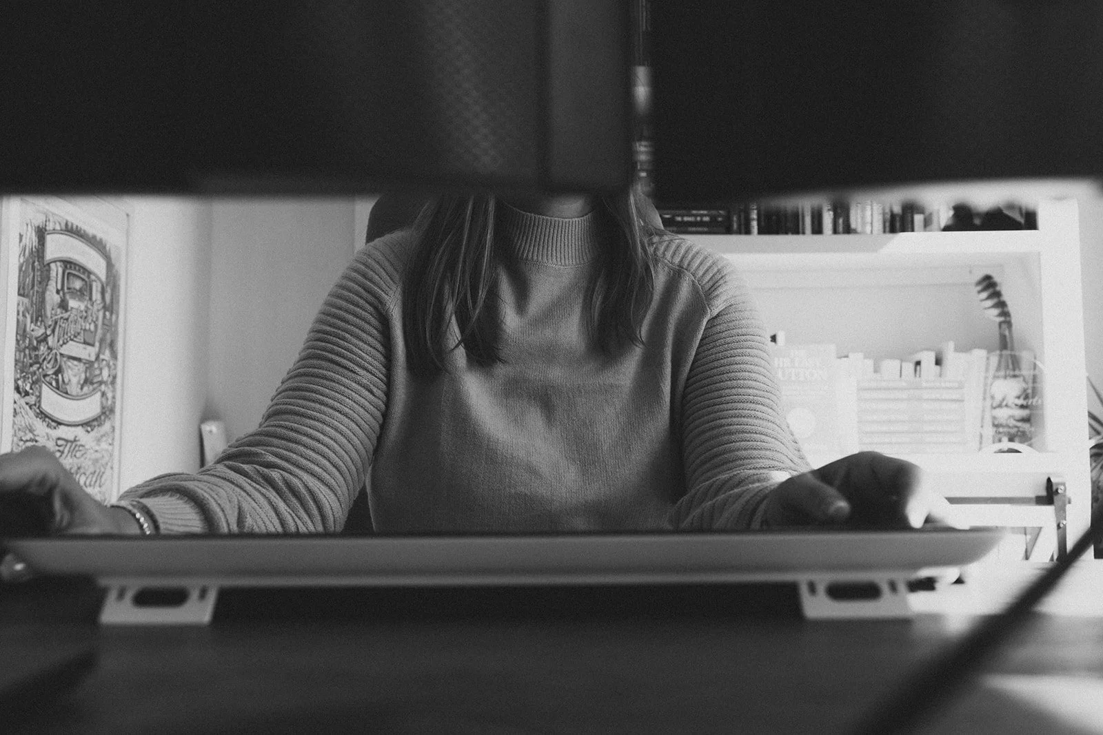 Black and white photo of Kerri M. Roberts, sitting at a desk, viewed from underneath a computer monitor.