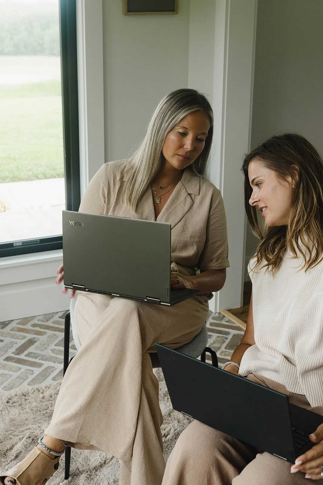 Kerri M. Roberts and a mentee, sitting indoors near a window, looking at laptops engaged in a discussion.