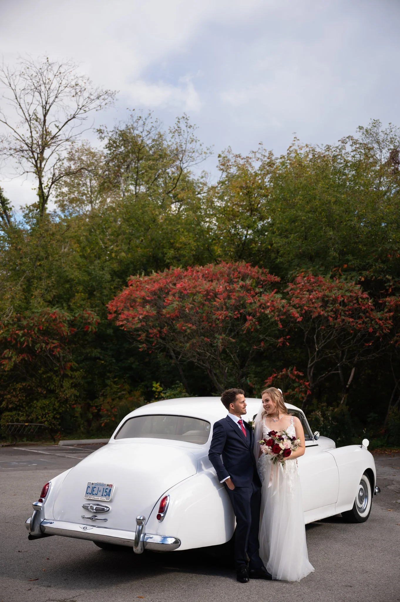 Bride and groom standing beside a vintage white car during their wedding portraits at Riverwood Park in Mississauga.