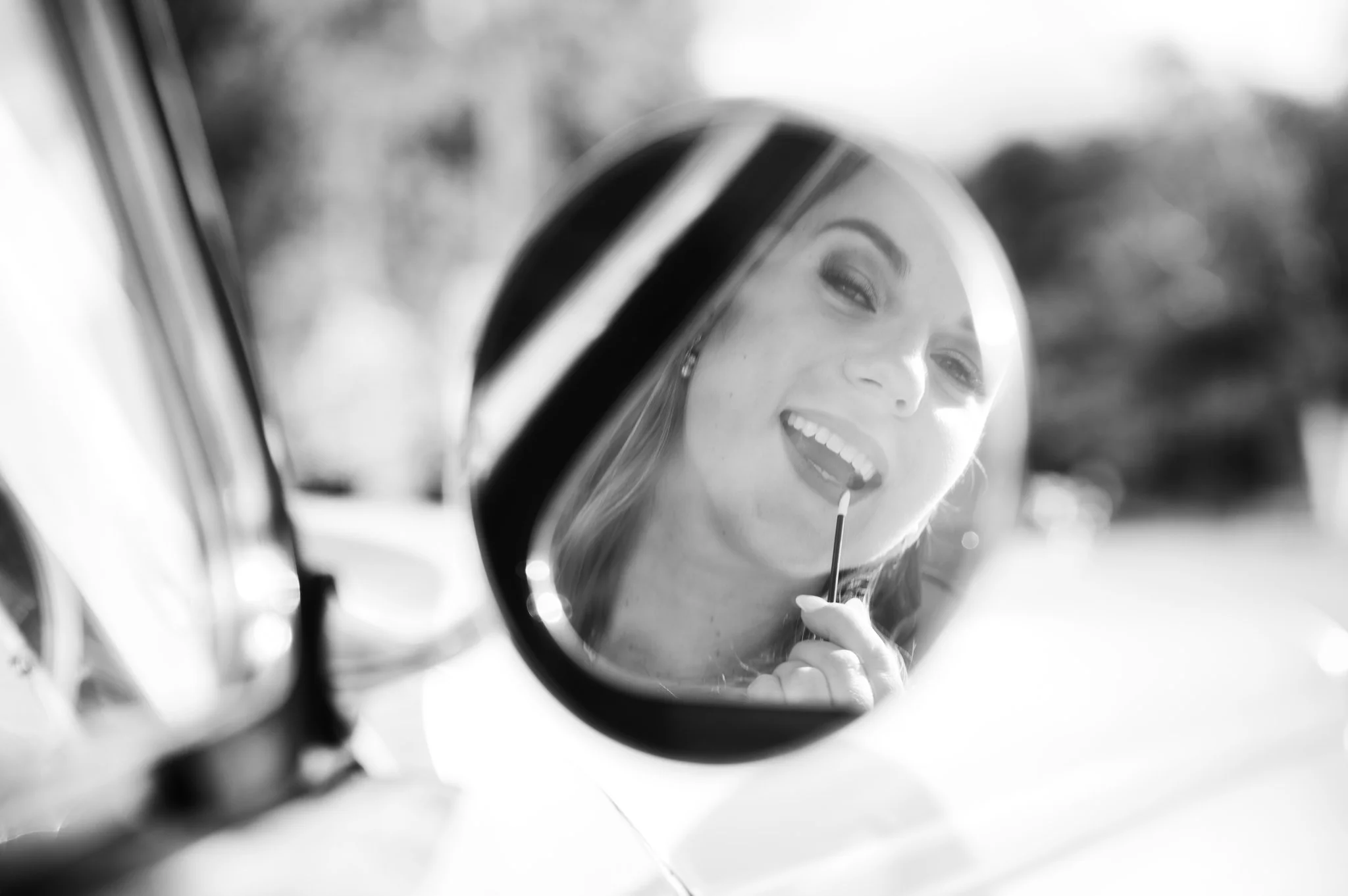 Bride touching up her makeup using a vintage car mirror during wedding portraits at Riverwood Park in Mississauga.