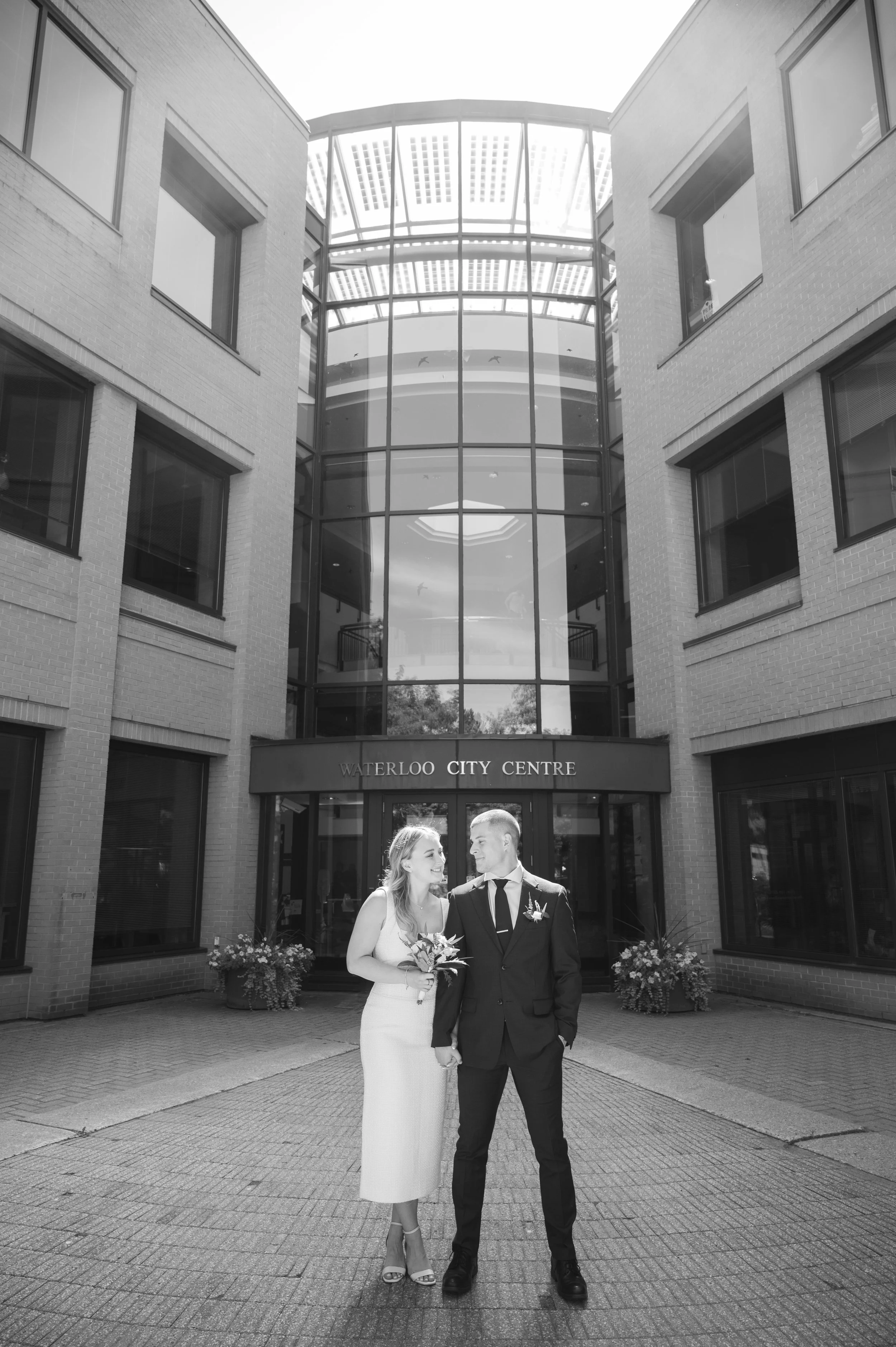 Bride and groom posing in front of a modern building entrance at Waterloo City Hall