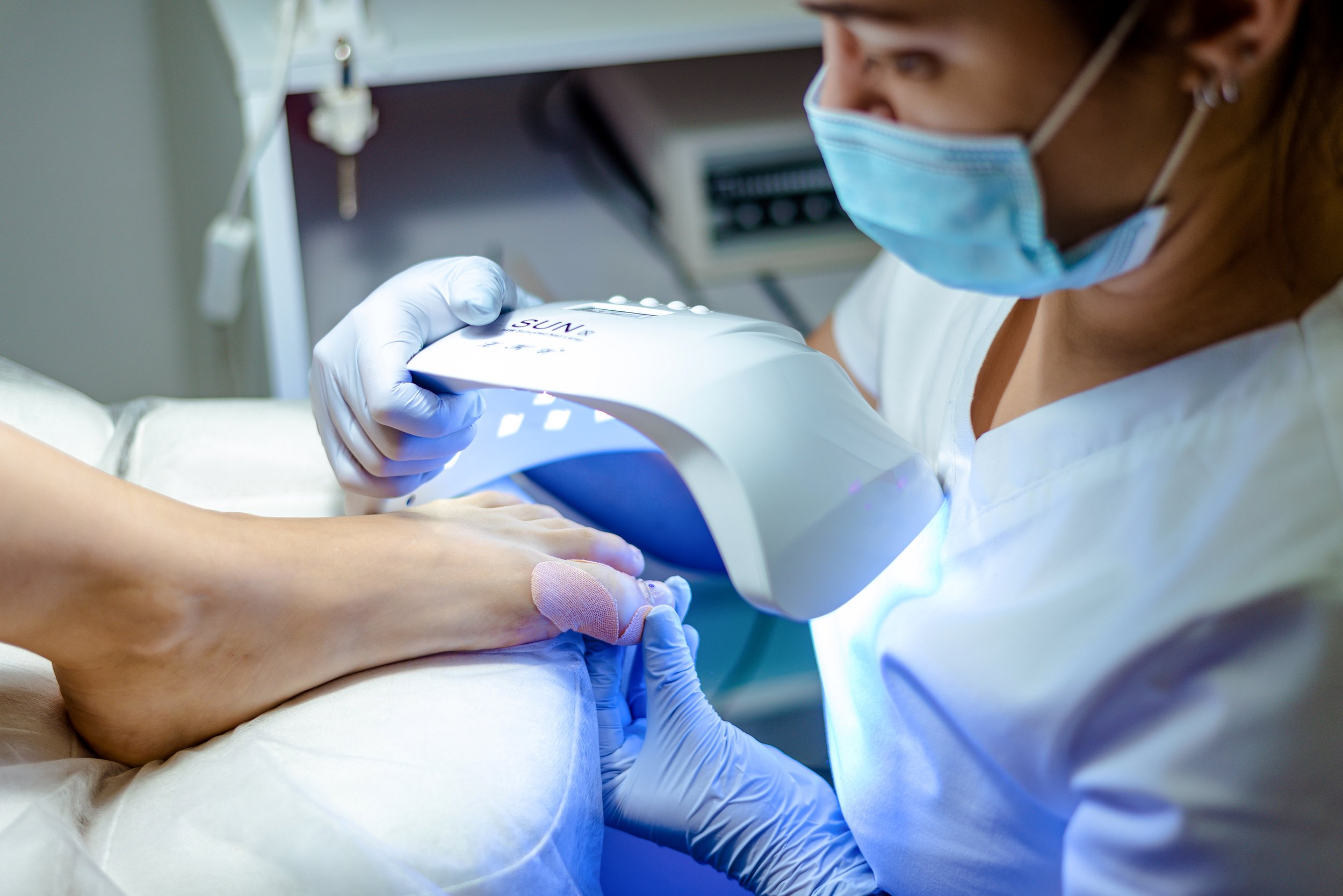 Healthcare professional in a mask and gloves performs a medical procedure on a patient's arm.