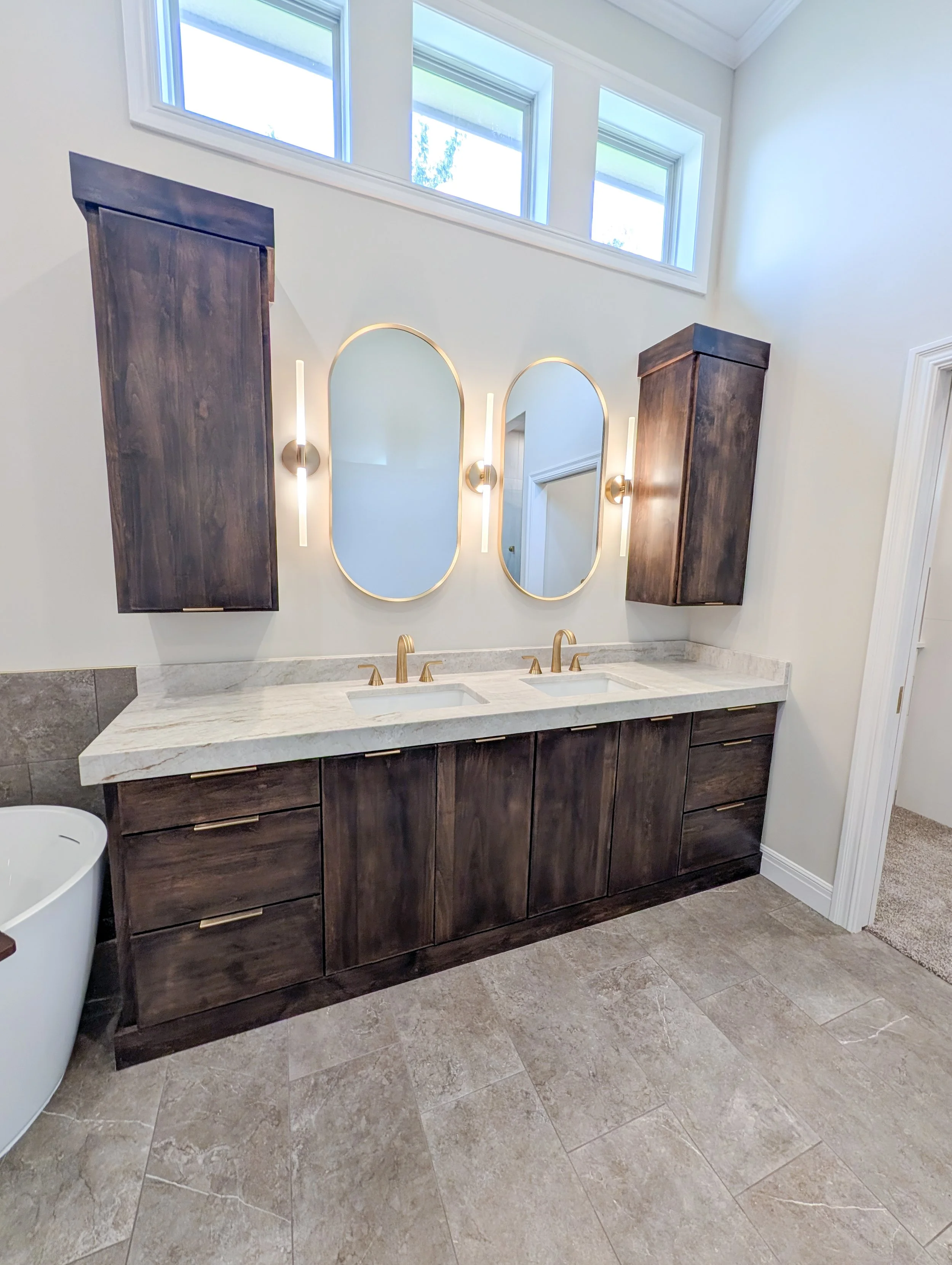 Custom dark wood double vanity with quartzite countertop, brushed gold faucets and oval mirrors