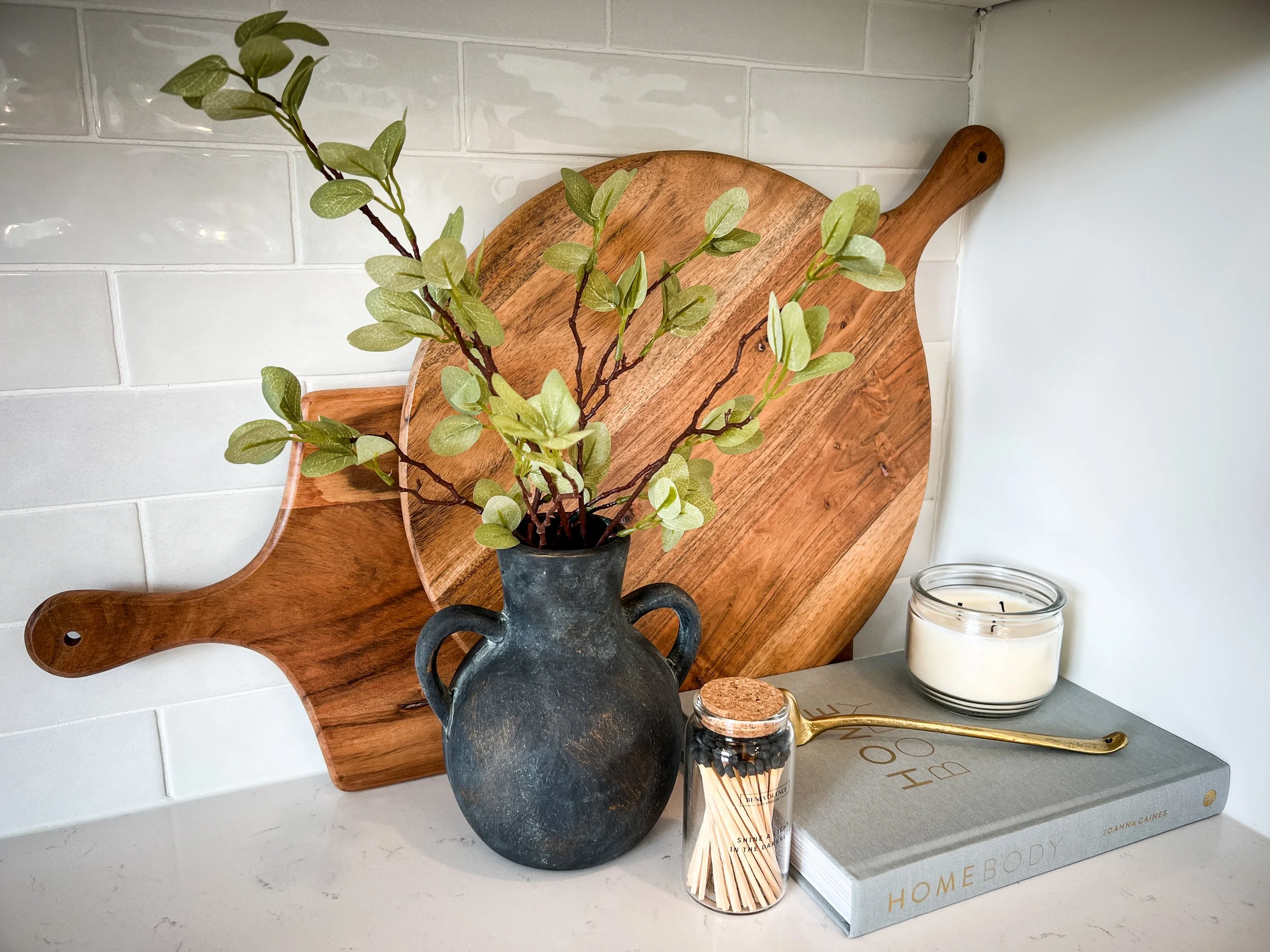 Kitchen counter styling with black vase, greenery, wooden cutting boards, and candle for modern Raymore home.