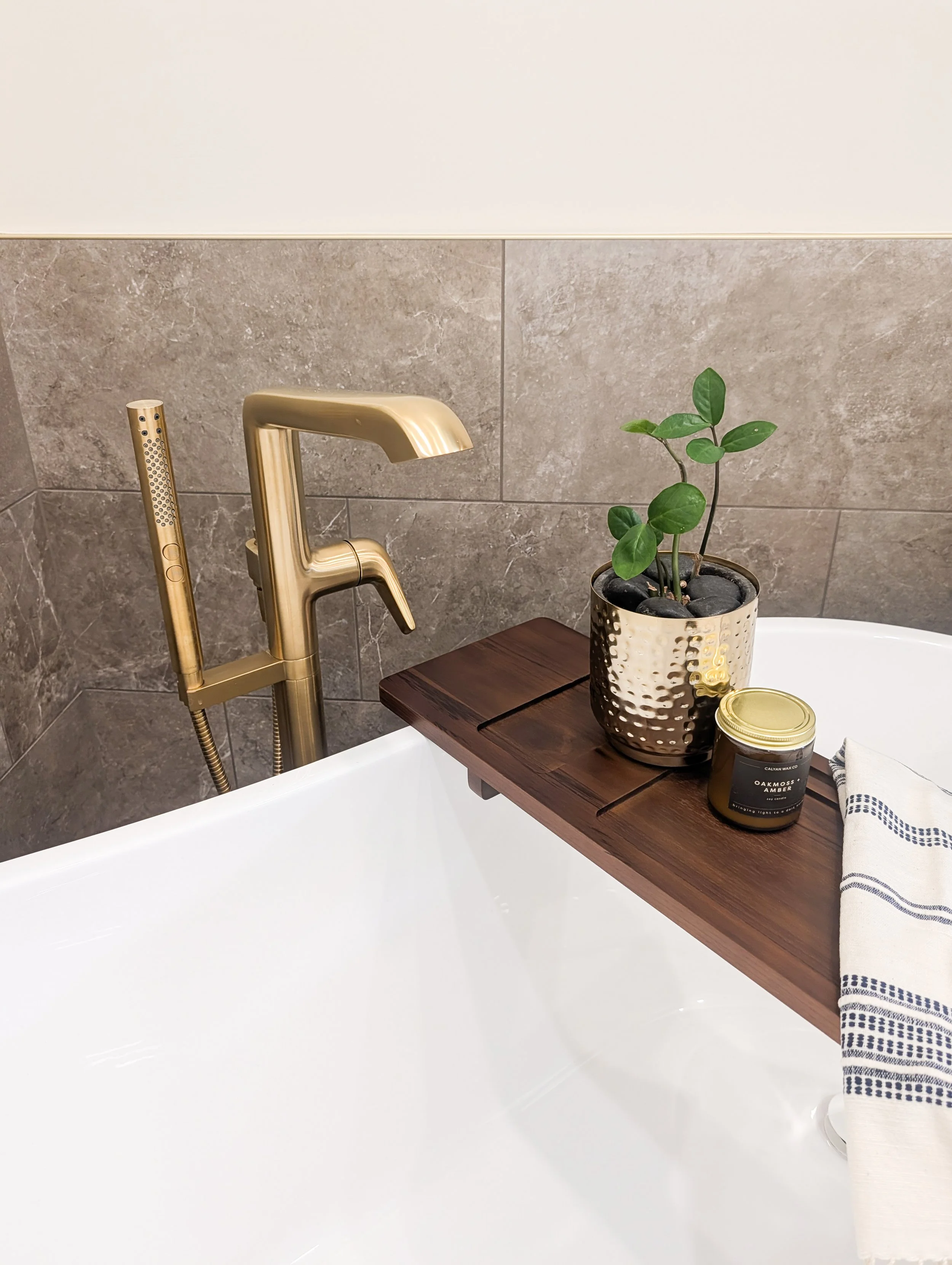 Close view of freestanding tub filler, tub tray candle and accent greenery with gold accents