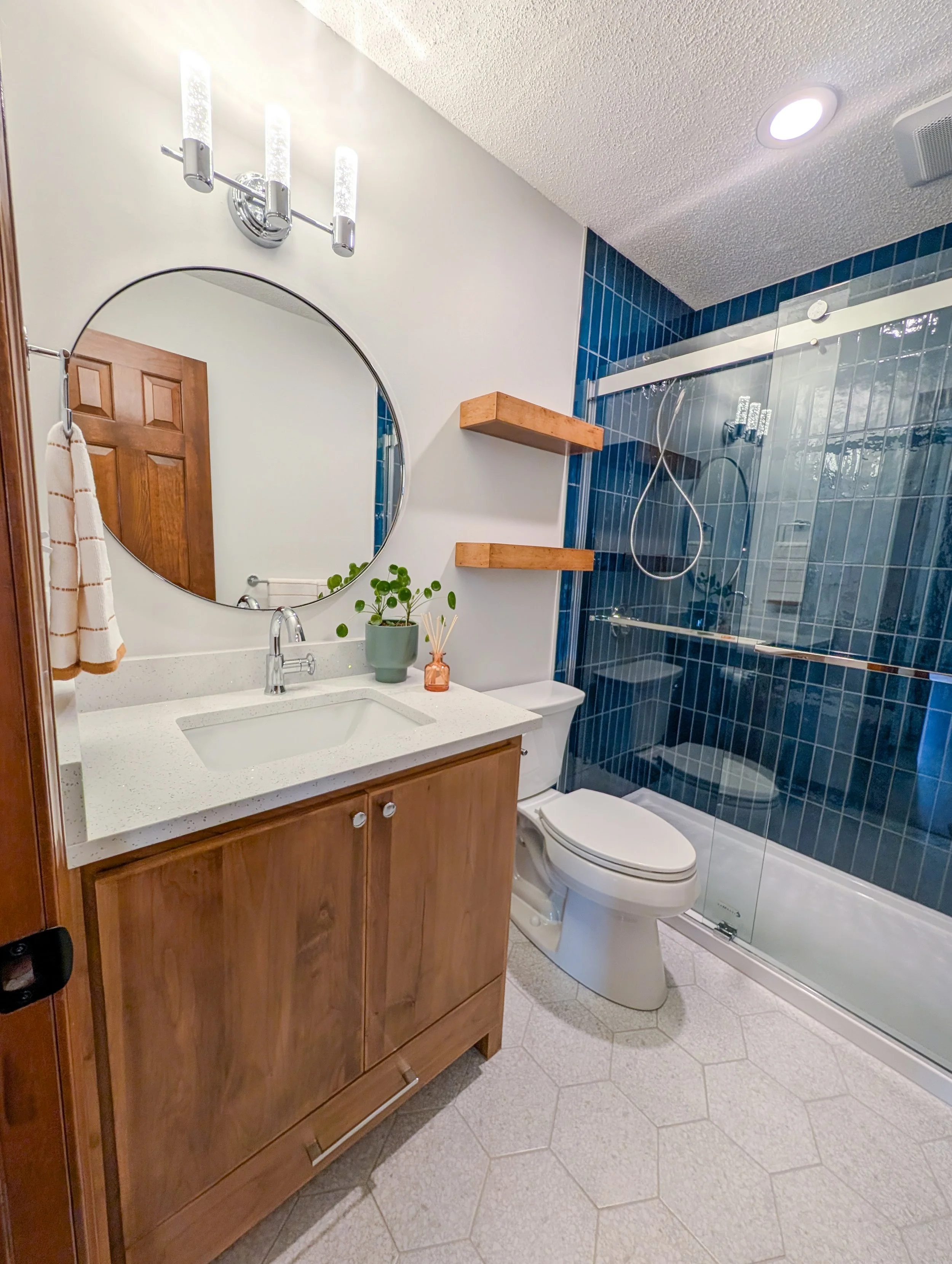 Lee's Summit hall bath remodel with wood cabinets, round mirror, blue shower tile and chrome finishes