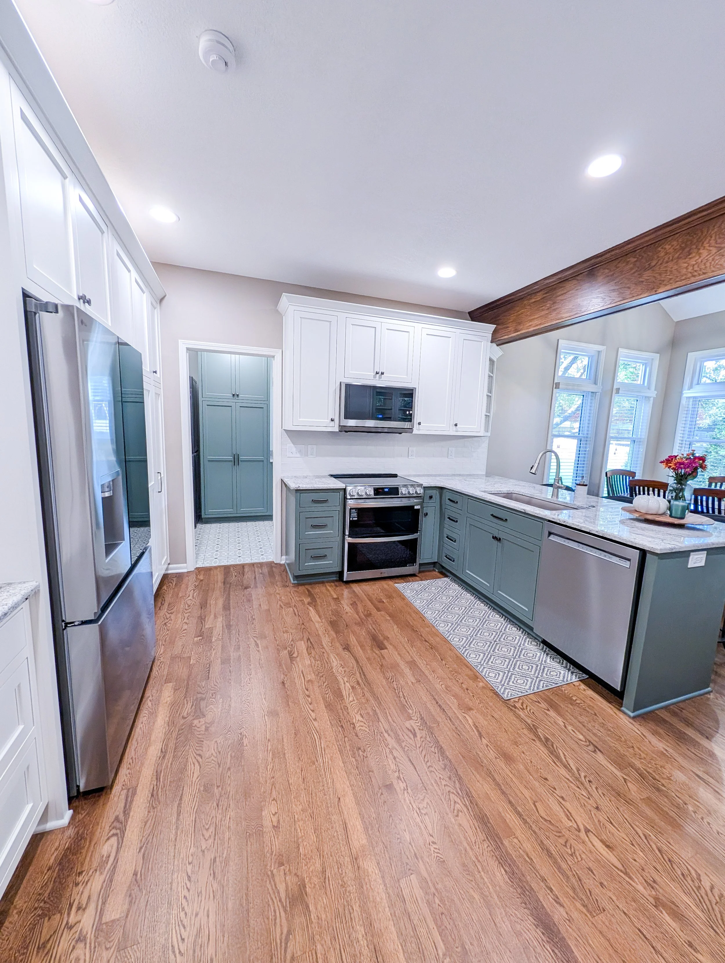 After photo of remodeled Lee’s Summit kitchen featuring two-tone white and green cabinets with new granite, and updated lighting.