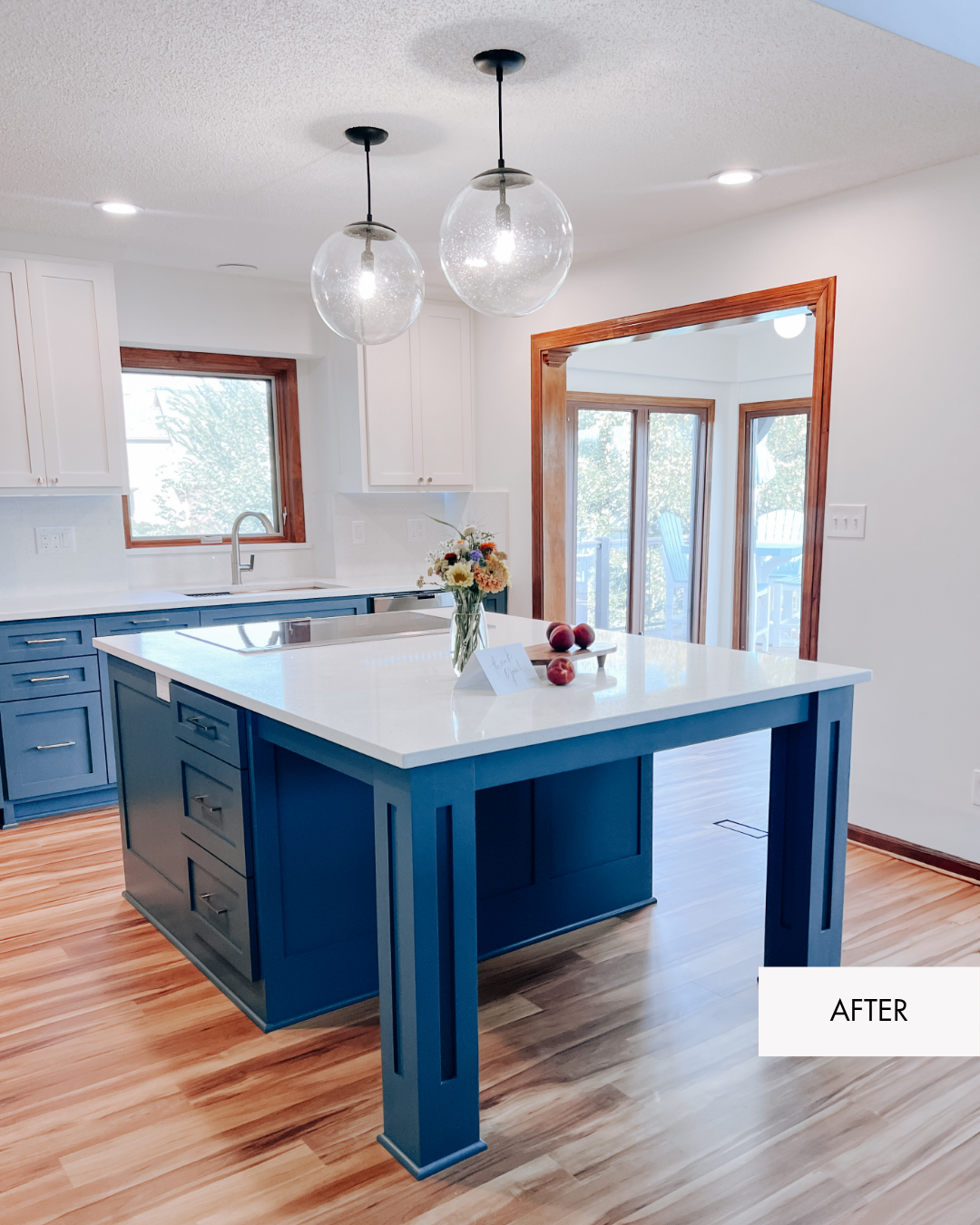 Remodeled Lee's Summit two toned kitchen with white walls, white upper cabinetry, blue lower cabinetry, black pendant lights, wood trim, MSI Sparkling White quartz countertops, new flooring and an open living room connection