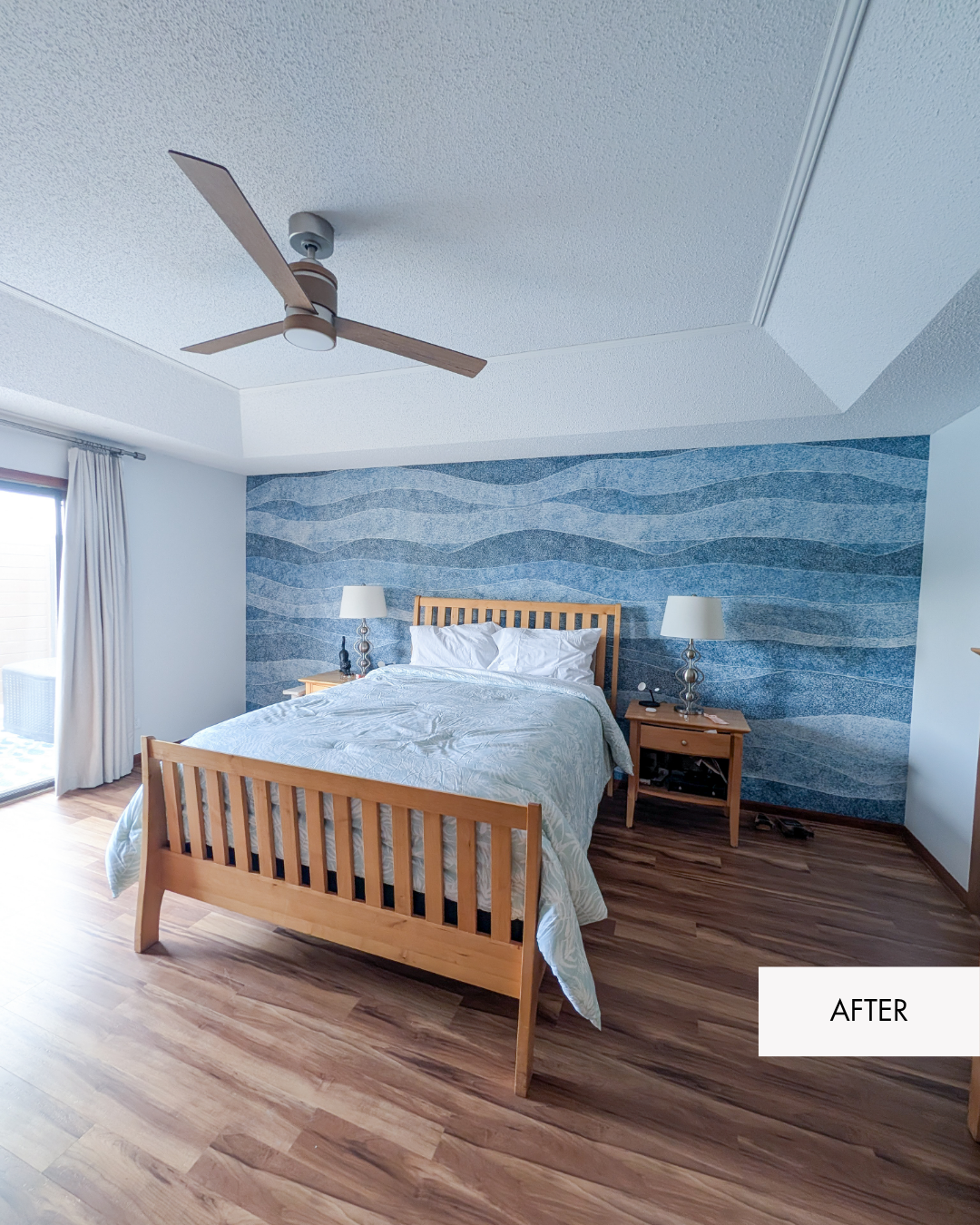 Remodeled primary bedroom with statement wallpaper, new flooring, updated paint, ceiling fan and drapery