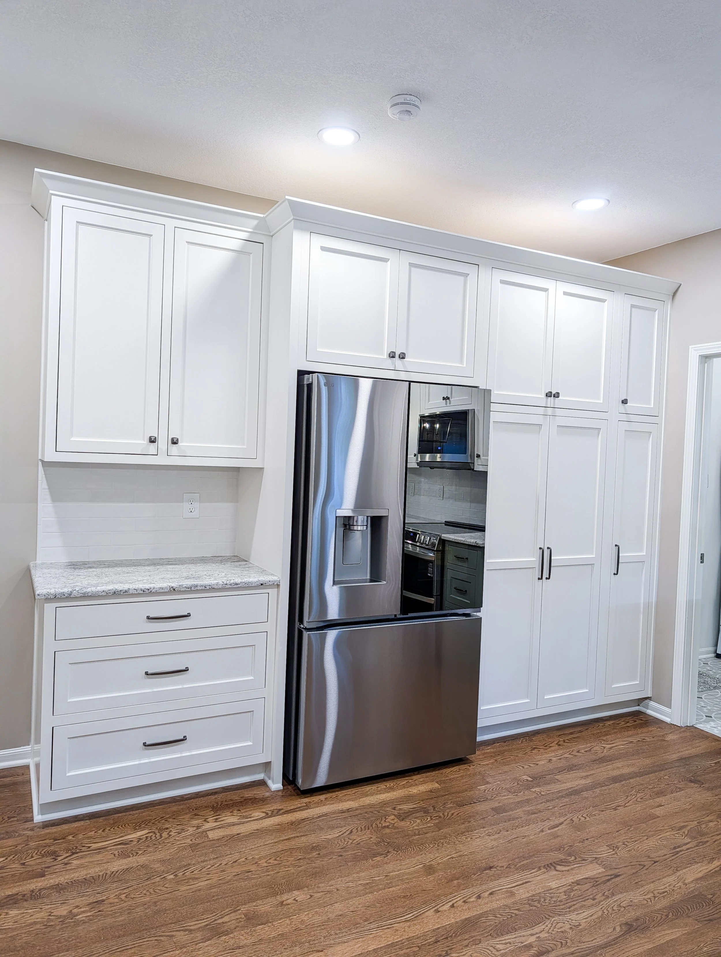 After photo of remodeled Lee’s Summit kitchen featuring two-tone custom cabinets in BM White Dove and SW Retreat, Salinas White granite, and updated lighting.