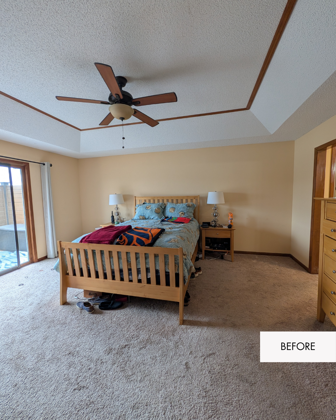 Primary bedroom before remodel with warm yellow walls, old carpet, old ceiling fan and 80's finishes