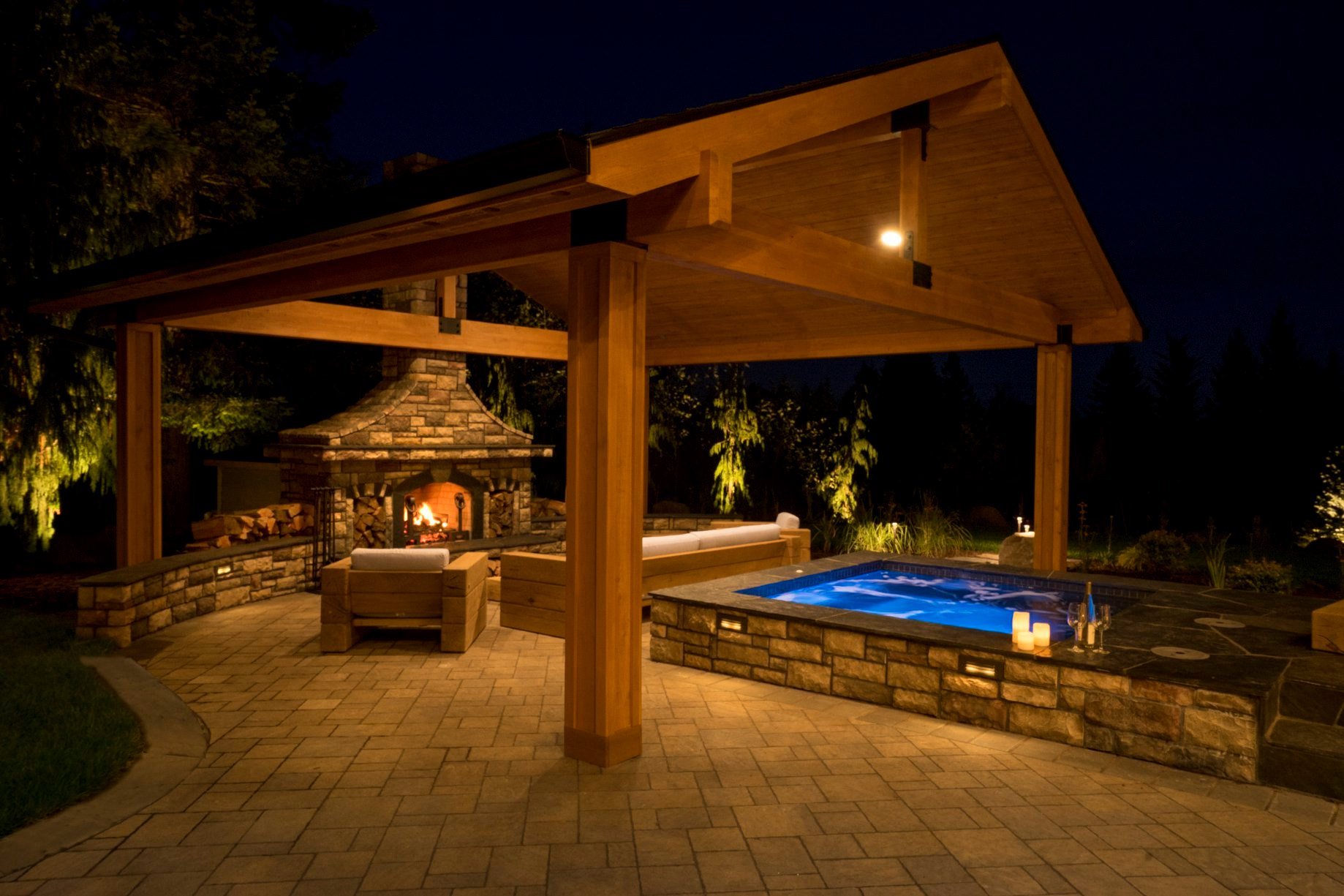 A luxury outdoor living space in Beaverton featuring a stone fireplace and an integrated hot tub under a custom timber pavilion, built by a beaverton landscaping company.