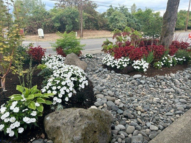 A gorgeous stone landscaping featured installed by Big Sky Landscaping using stones, boulders, mulch, local fauna, and white flowers. 