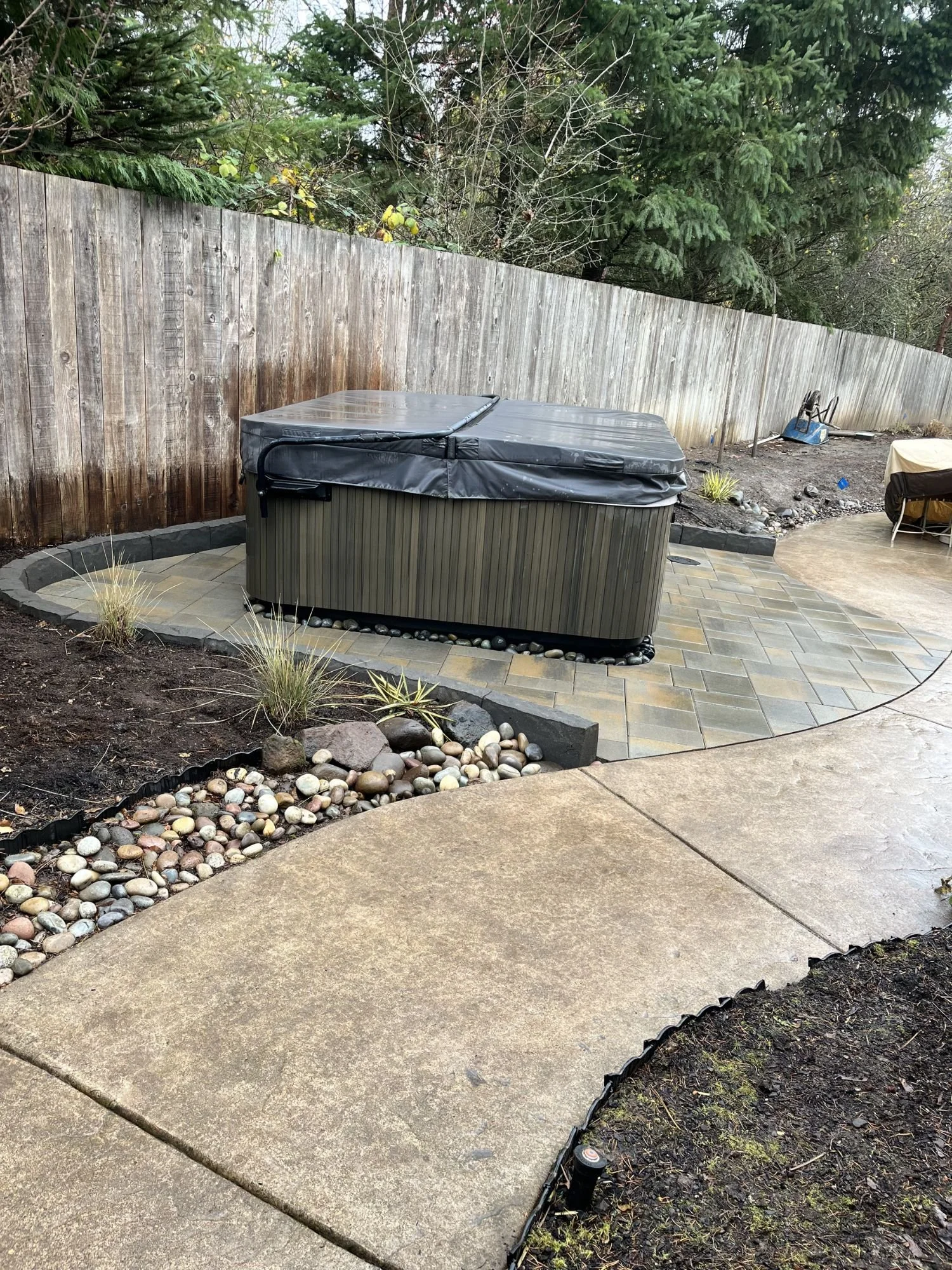 A hot tub sitting on a block stone patio with a concrete paver and fresh landscaping surrounding it. 