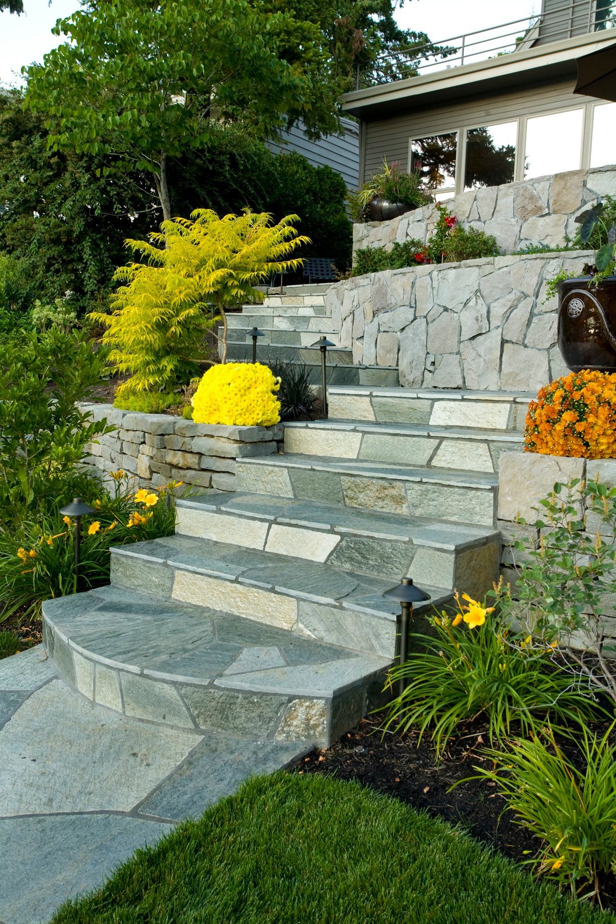 Natural flagstone stairs wind through a tiered garden featuring lush greenery and bright yellow blooms at a home in Beaverton.