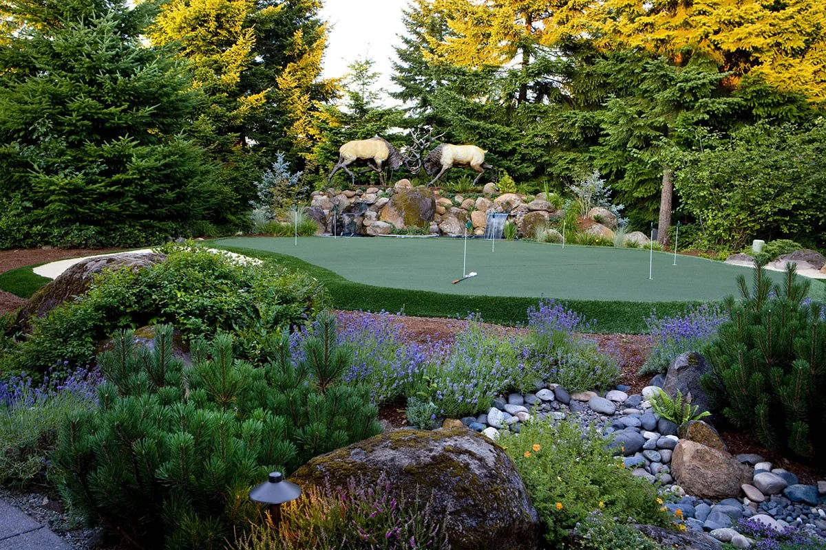 A custom backyard putting green in Wilsonville is accented by a natural rock water feature and life-sized elk sculptures.