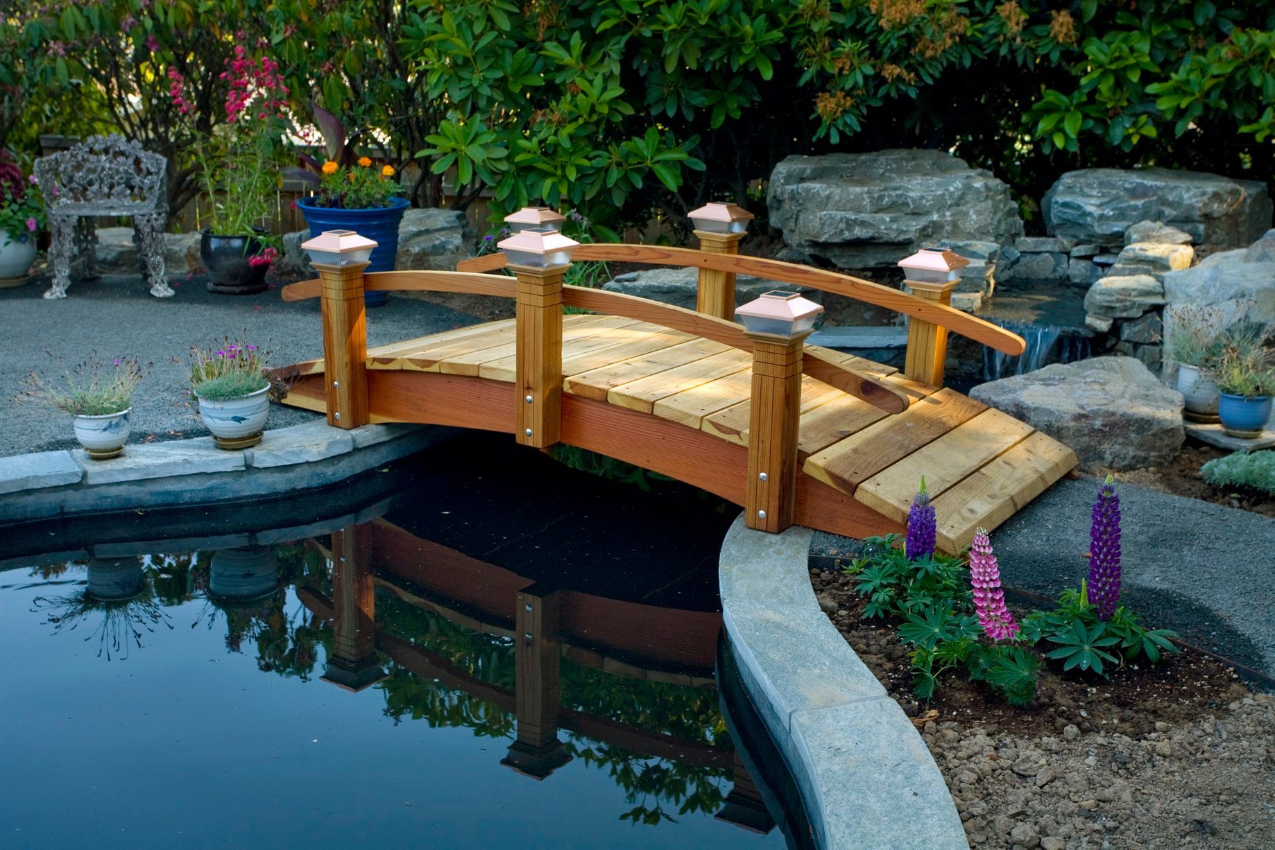 A custom wooden arched bridge crosses over a tranquil garden pond in a professional Oregon City landscape design.