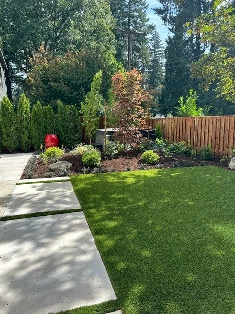 A pristine Tigard backyard transformation featuring artificial turf, a concrete path, and a new cedar privacy fence.