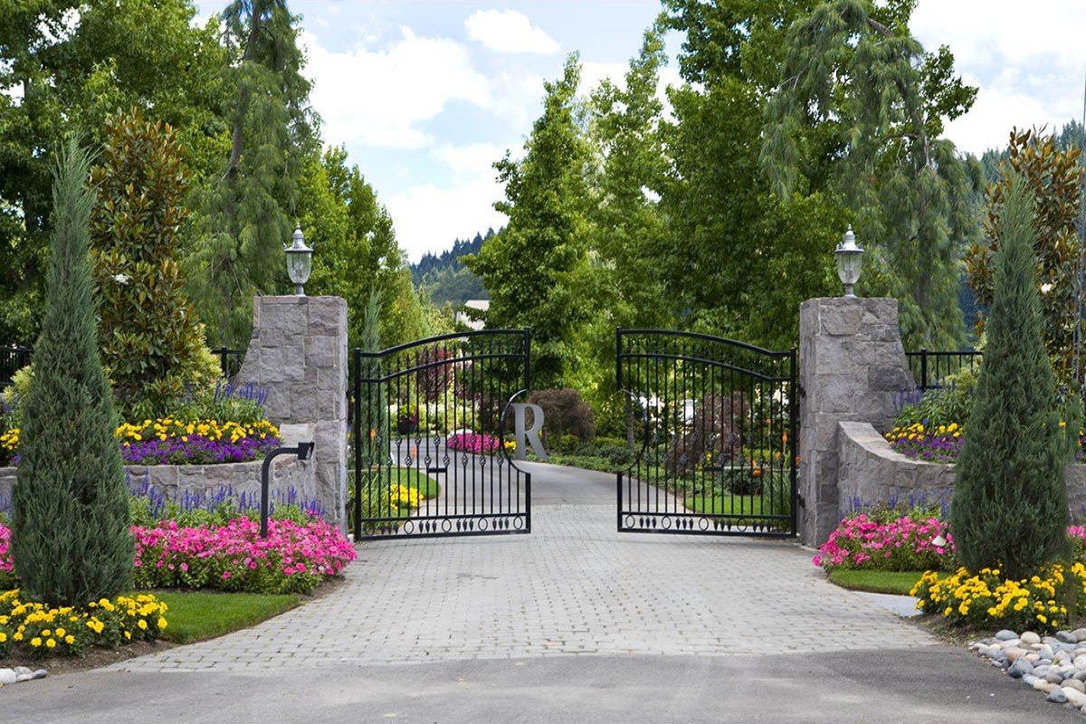 An elegant gated entrance featuring stone pillars and vibrant flower beds designed by a premier beaverton landscaping company.