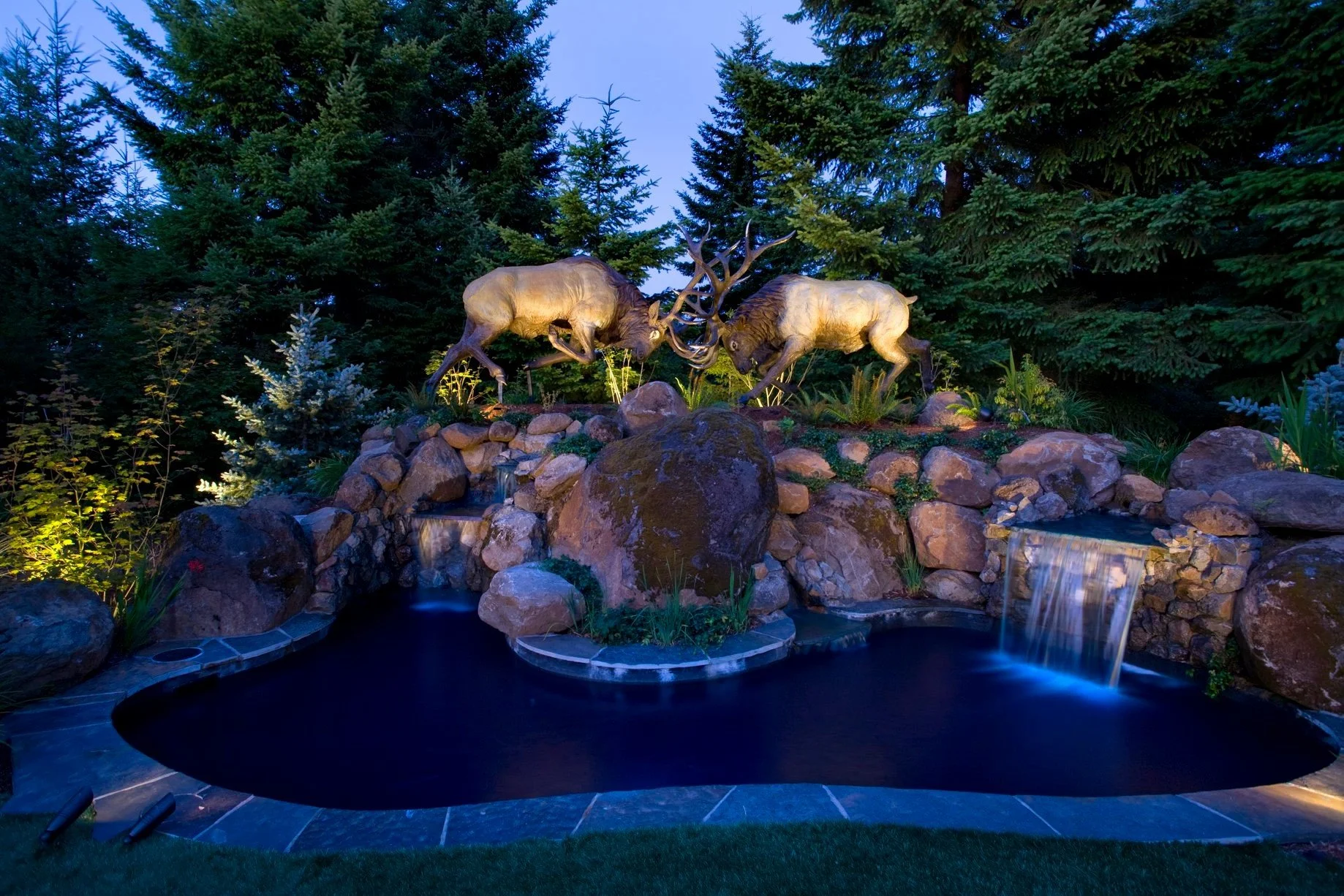 A dramatic nighttime water feature in Oregon City showcases a custom elk sculpture and cascading waterfalls designed by expert Oregon City landscapers.