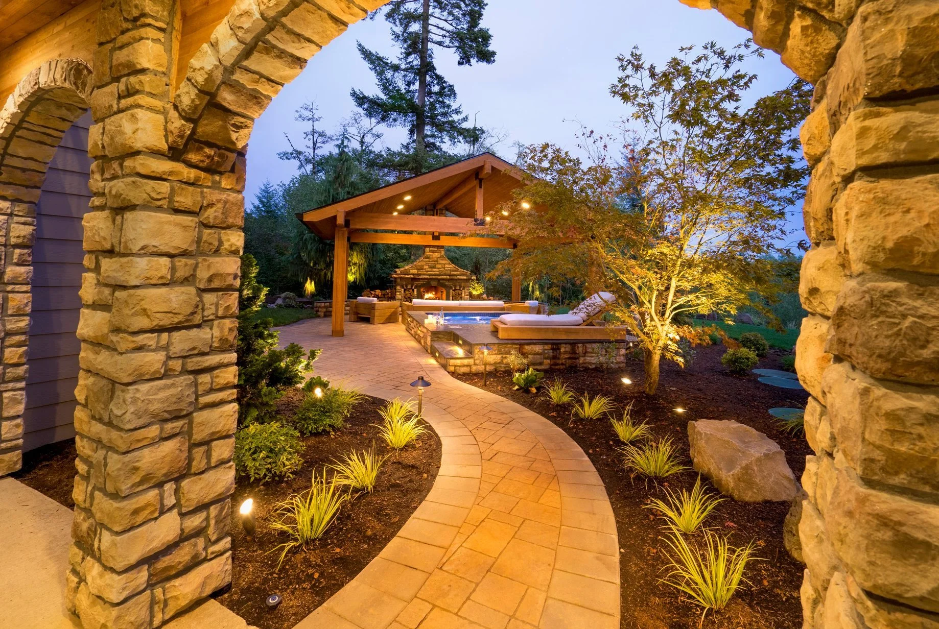 A curved paver path leads toward a beautiful wood and stone pavilion at a luxury residence in Hillsboro.