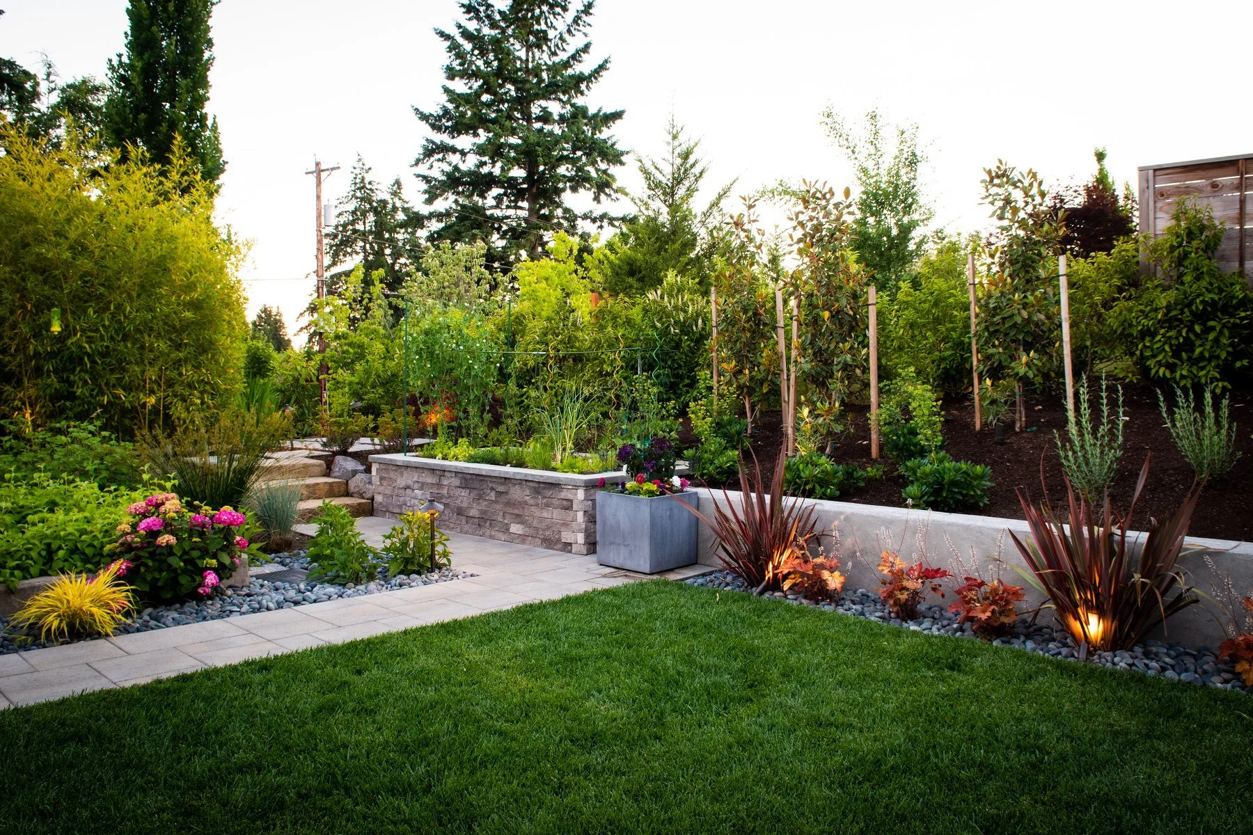 This layered landscape design in Hillsboro features concrete and stone retaining walls, stylish metal planters, and strategic lighting.