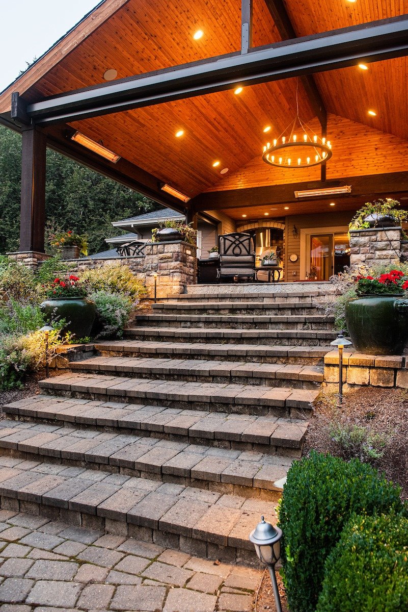 Dramatic stone steps lead up to a grand timber-framed outdoor living area with custom lighting and heating at a Wilsonville residence.