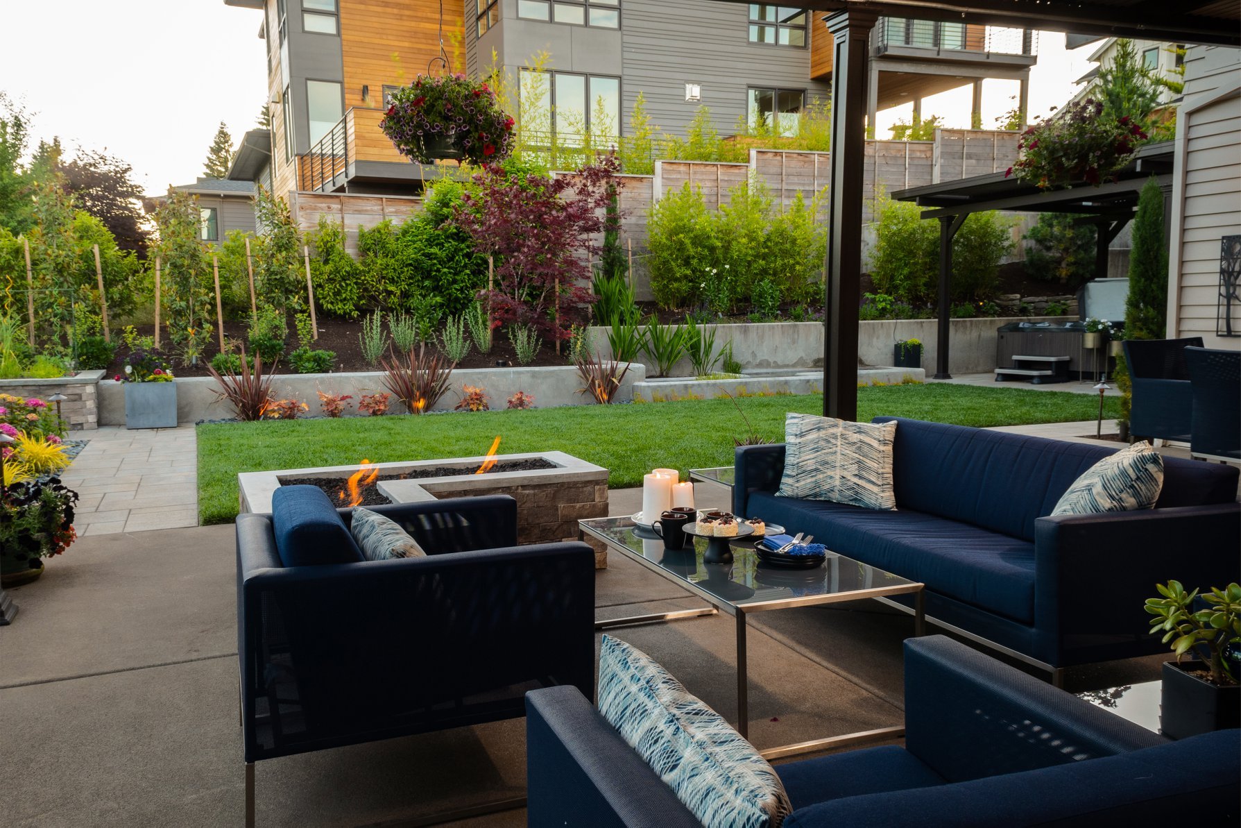 An upscale outdoor patio in Oregon City featuring deep blue sofas, a modern fire pit, and professional lighting by a top Oregon City landscaping company.