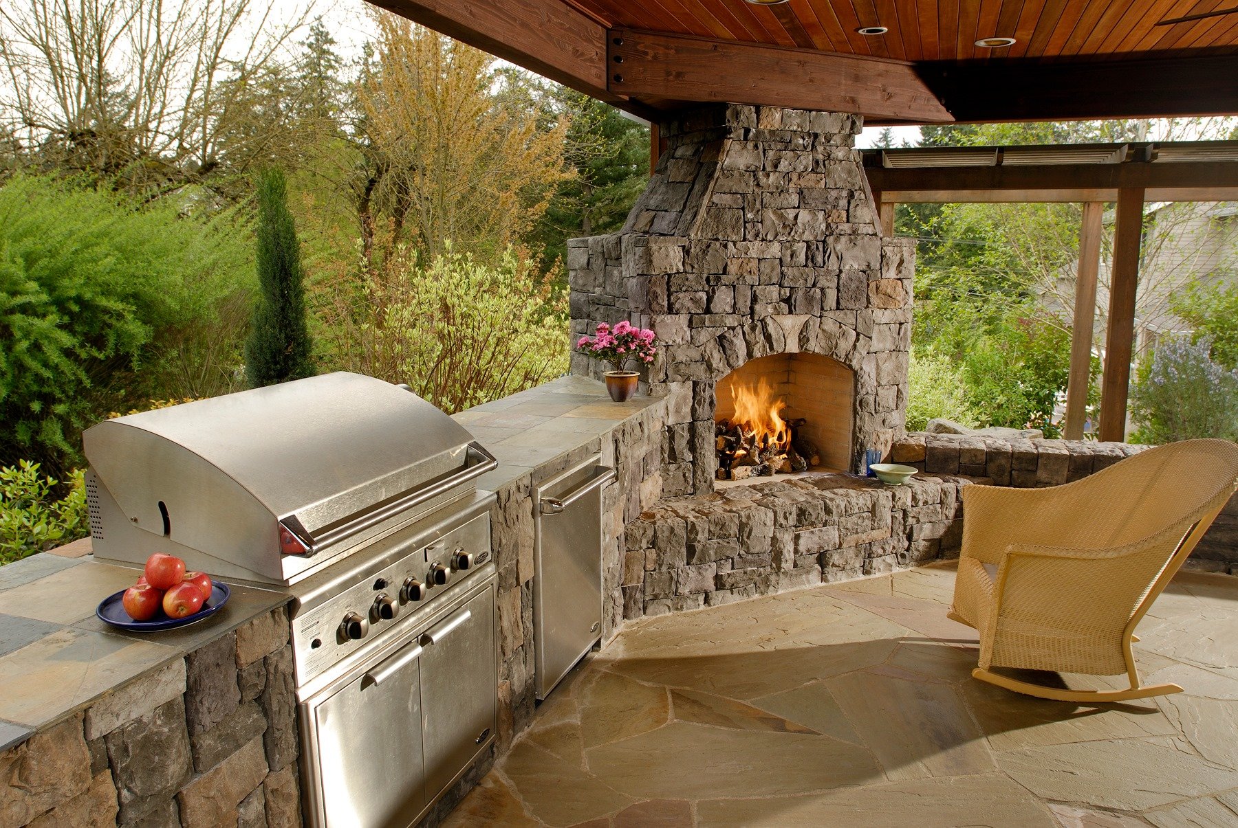 An outdoor stone kitchen in Hillsboro features a stainless steel grill and a cozy fireplace, all designed by a leading Hillsboro landscaping company.