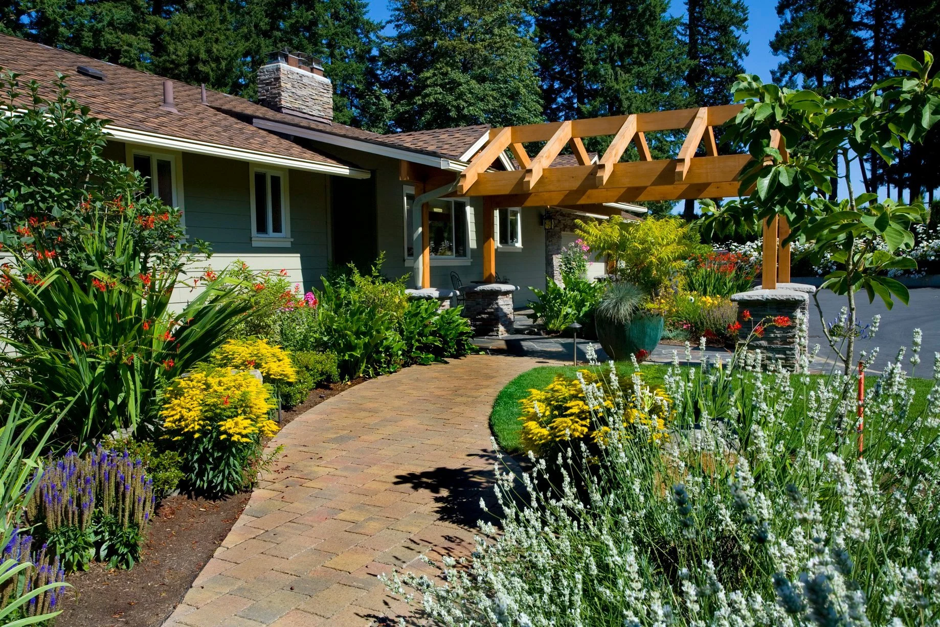 A charming paver walkway leads to a custom timber-framed entryway at a home in Oregon City, surrounded by lush perennial gardens.