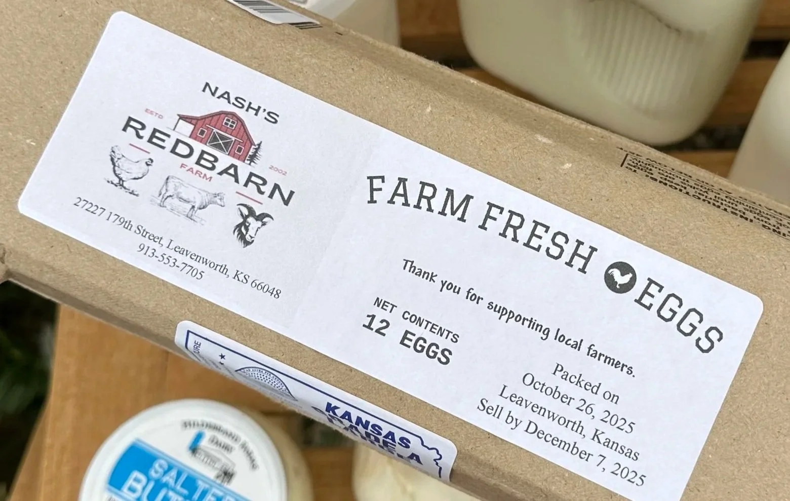 A cardboard box with a label from Nash's Red Barn Farm that sells farm fresh eggs, supporting local farmers, containing 12 eggs, packed in Leavenworth, Kansas.