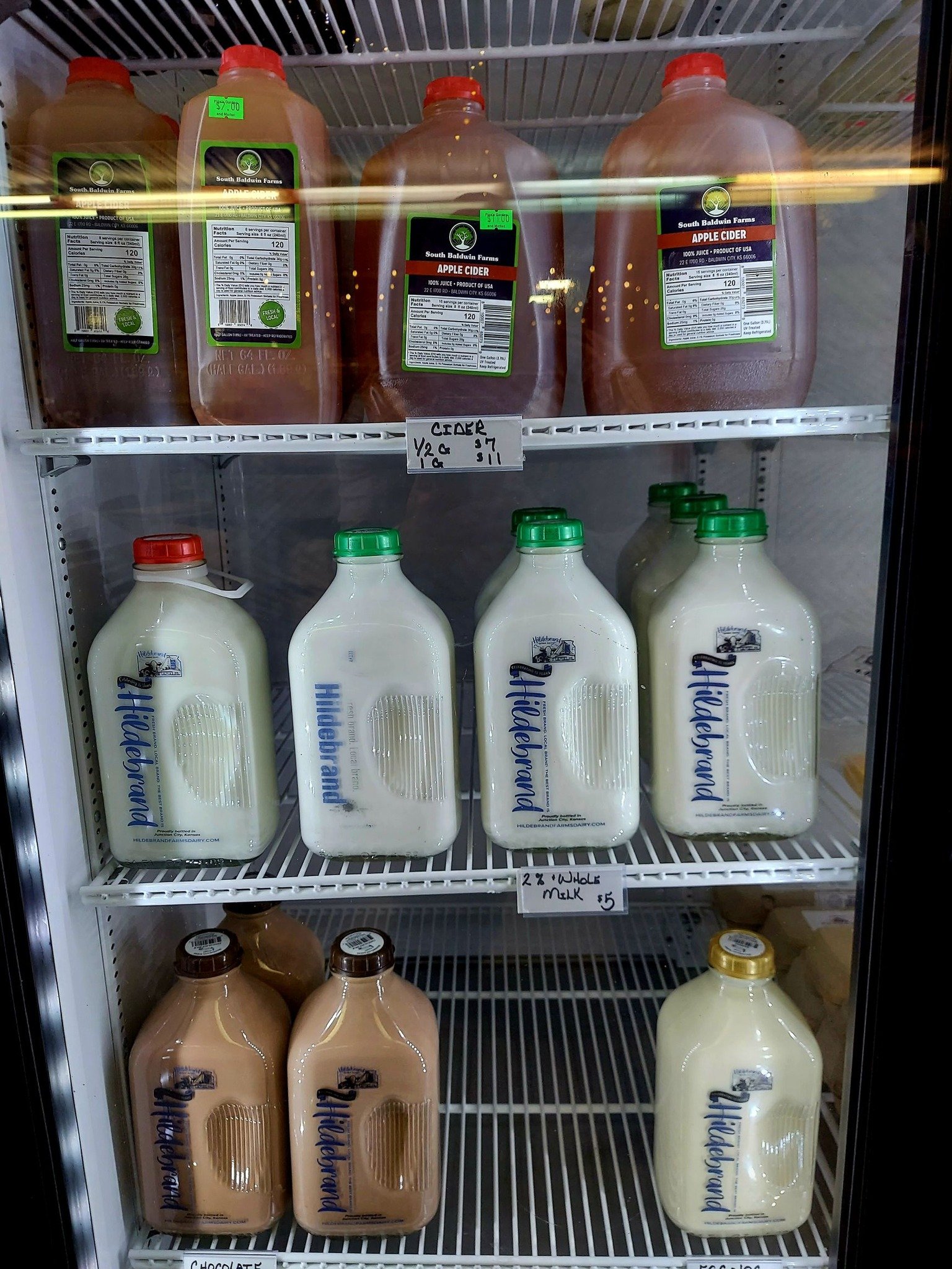 Various bottles of dairy products and beverages in a refrigerator, including apple cider and milk in different flavors.