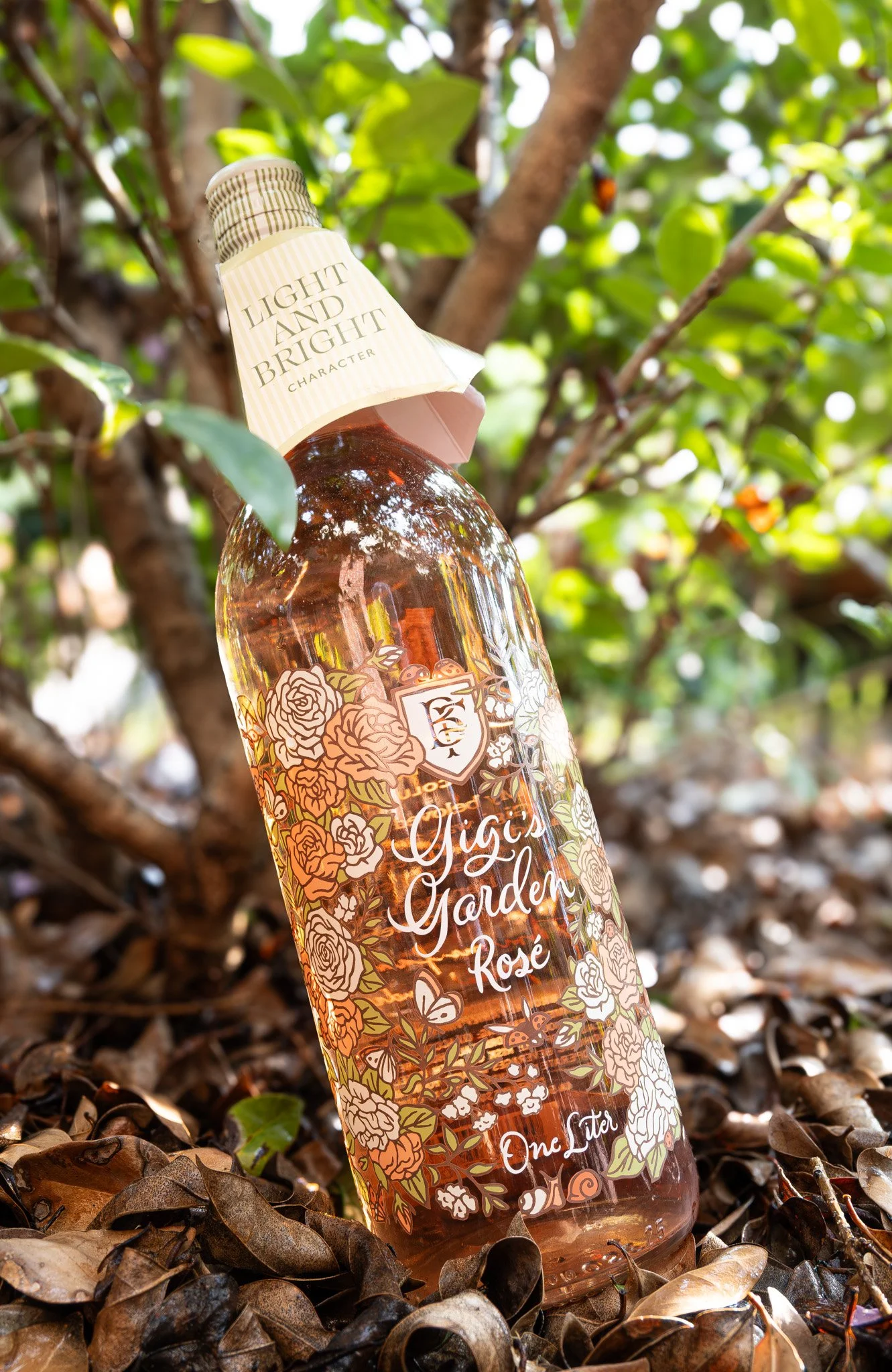 A bottle of rosé wine labeled 'Yiga Garden Rosé' resting on a bed of leaves with a tree and green foliage in the background.