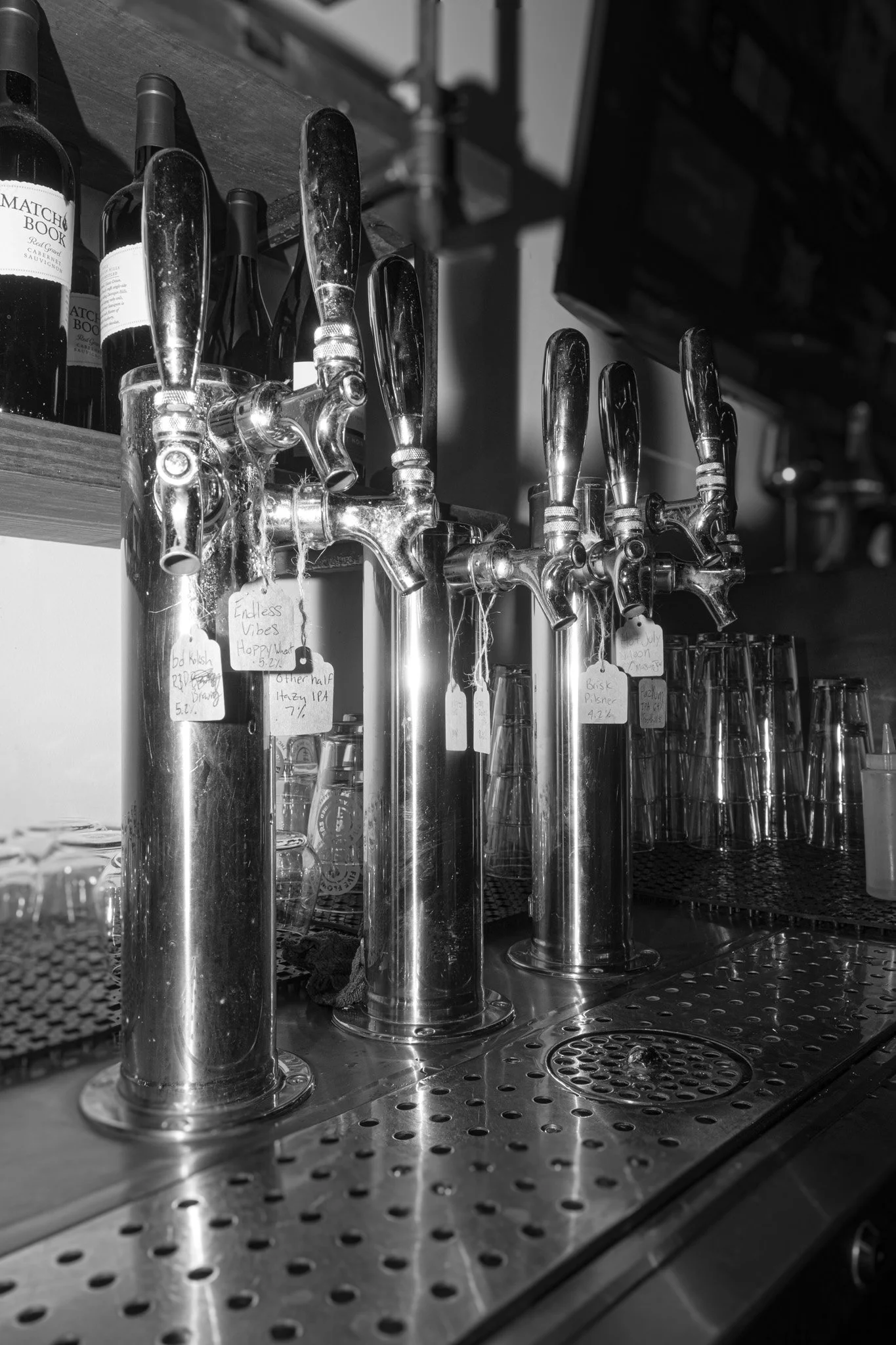 Black and white photo of beer taps with tags hanging on them in a bar or brewery.