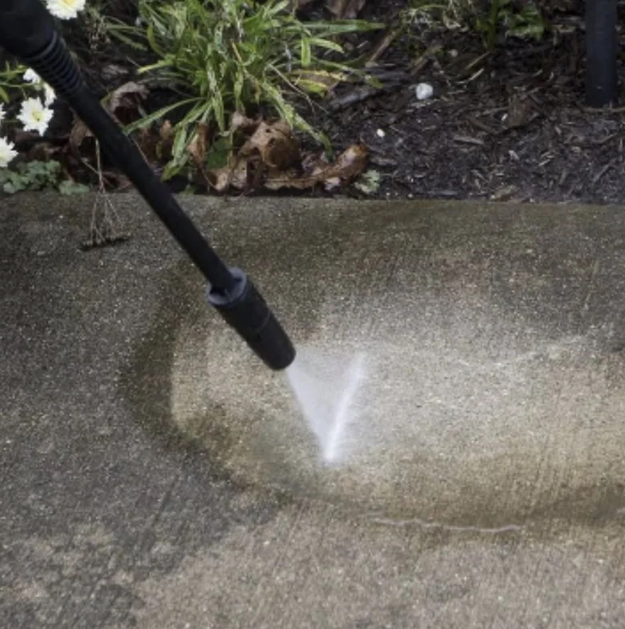 Pressure washing a concrete surface near a garden.