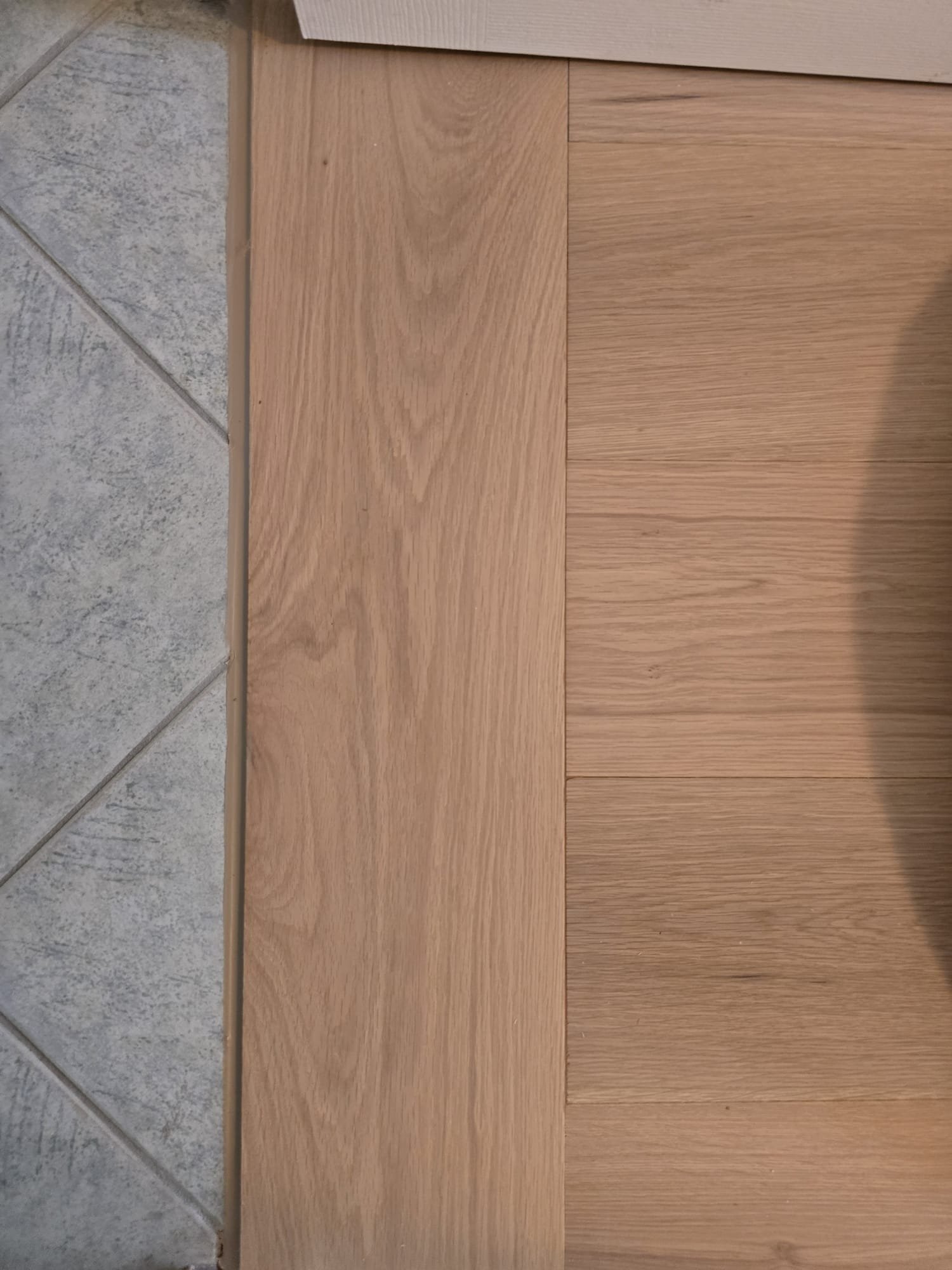 Person installing wooden flooring in an unfinished room with white walls and exposed wires.