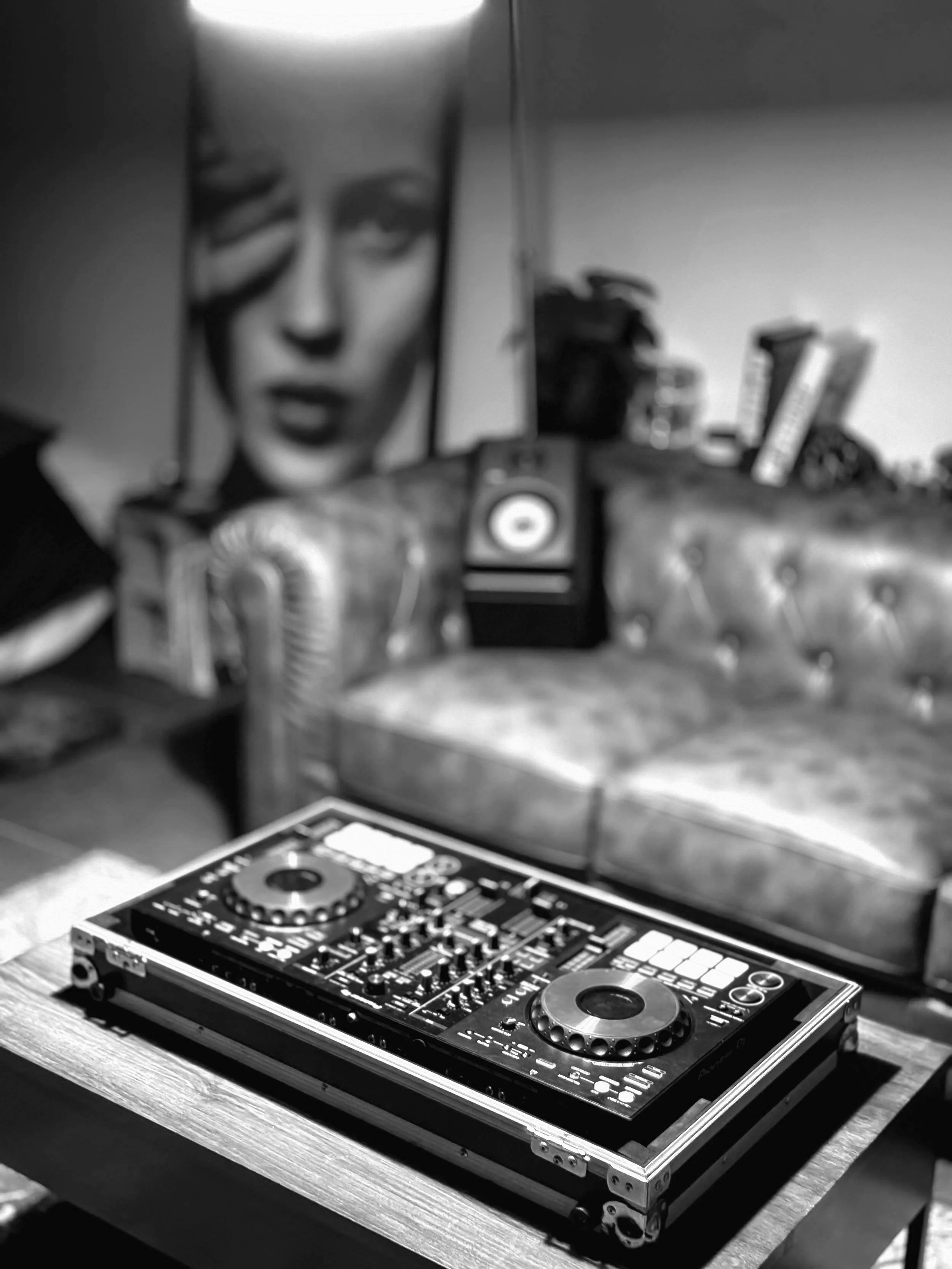 Mesa con equipo de DJ, fondo con retrato en blanco y negro y sillón de cuero.