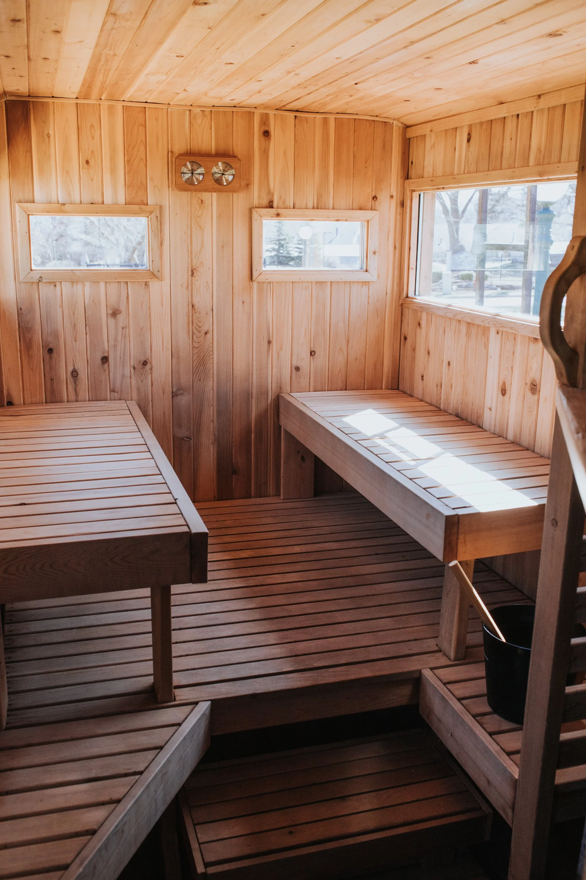 A small, enclosed wooden sauna with benches along the walls and windows letting in natural light.