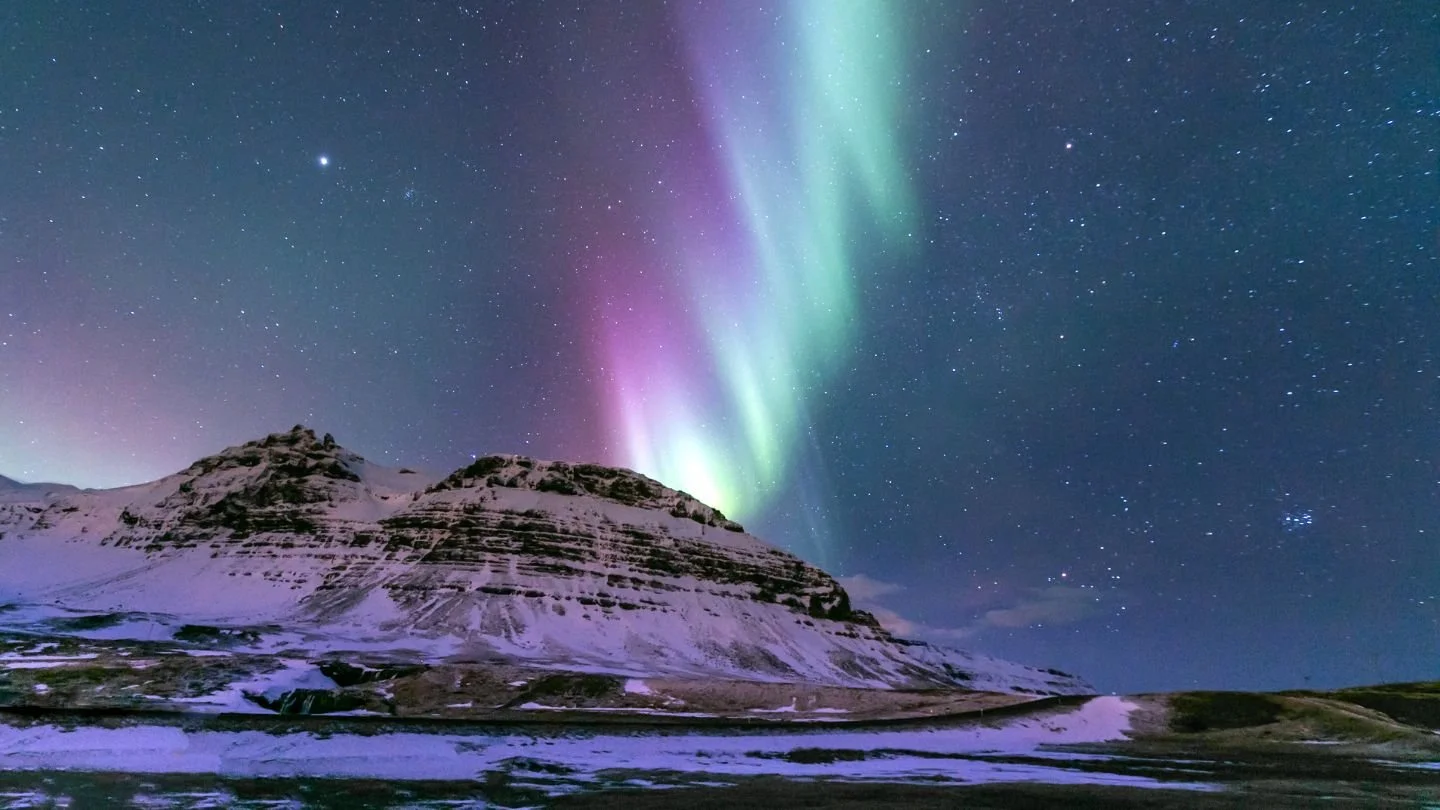 Northern lights over a snow-covered mountain at night with stars in the sky.
