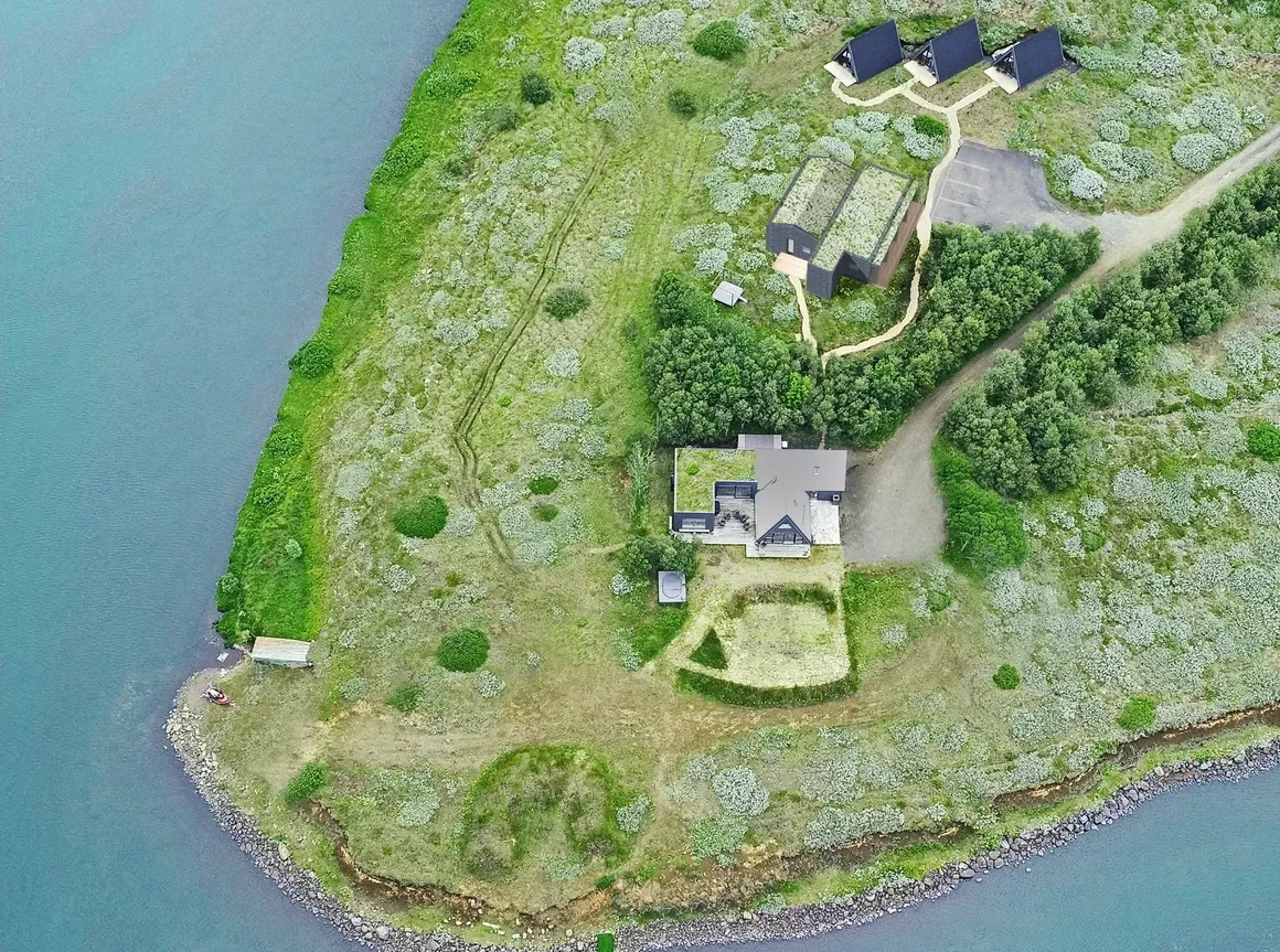 Aerial view of a coastal property with multiple buildings, a large house, and surrounding greenery.