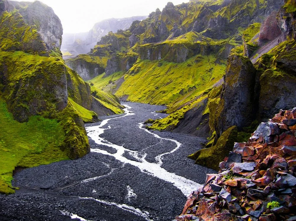 A fjord landscape with moss-covered cliffs, a winding river, and a rocky foreground.