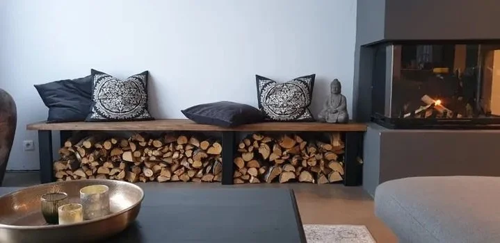 Living room with a wood storage bench with pillows, a small statue, a modern fireplace, and part of a gray sofa.