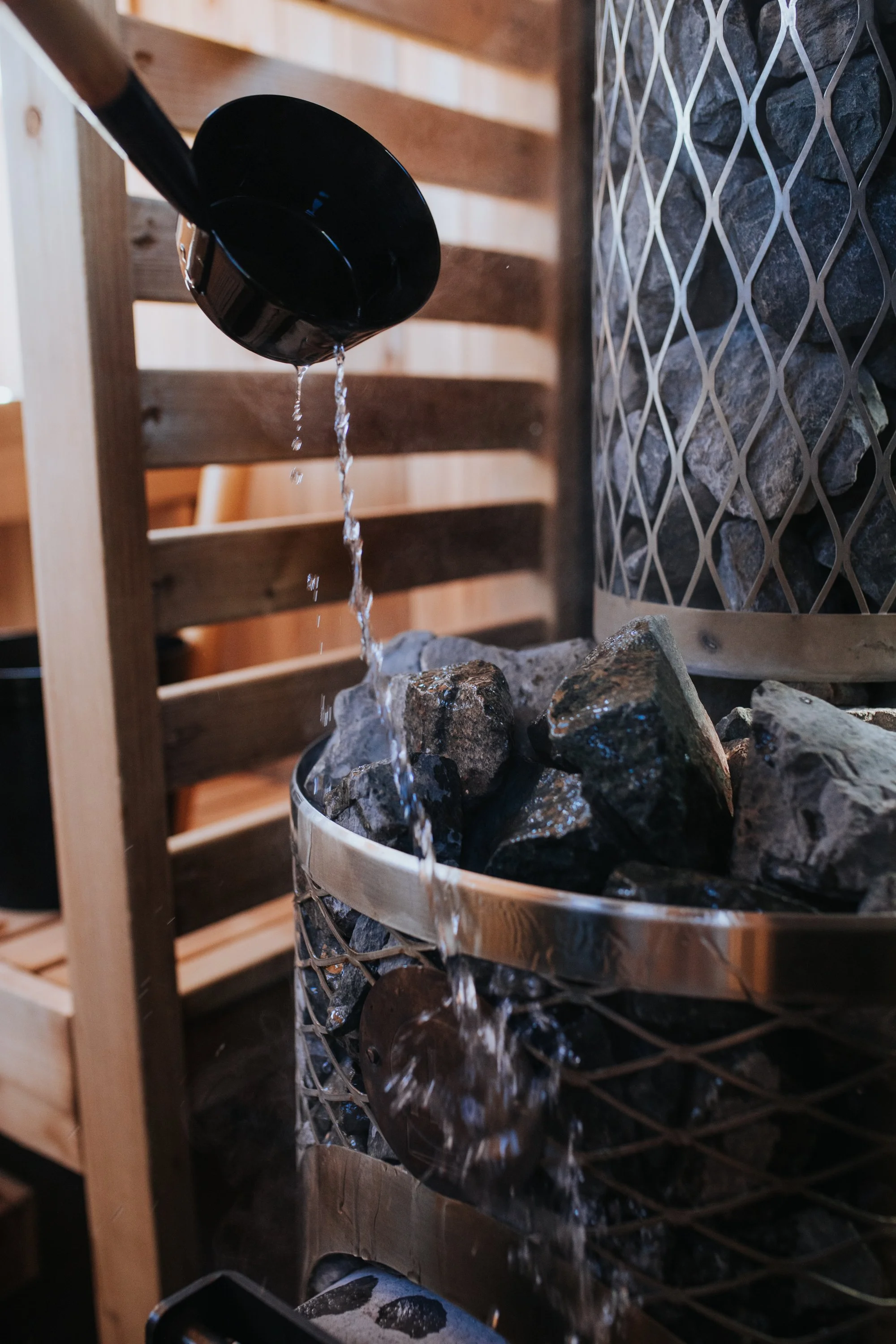 A modern sauna stove with glowing fire inside, branded 'iki' with a metal and rock exterior.