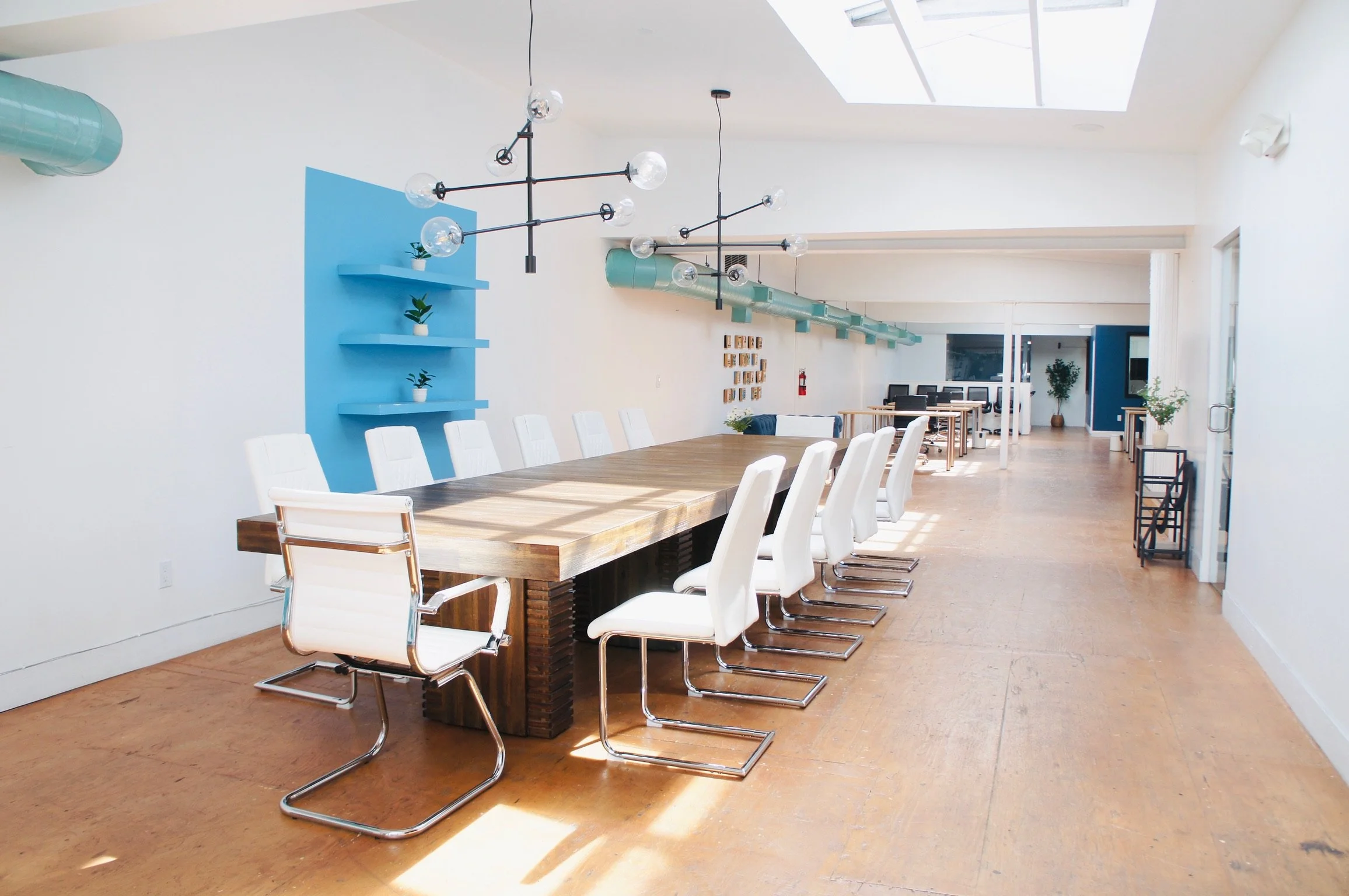 Empty modern conference room with a long wooden table, white chairs, and sunlight streaming through skylights.