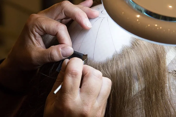 A craftsperson placing individual hairs into a custom hair system base.