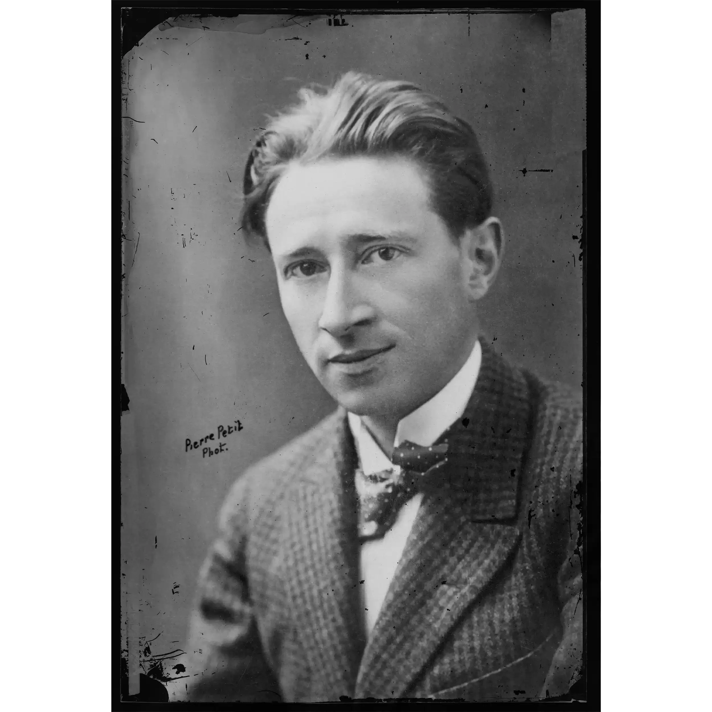 Black and white photograph of a young man with styled hair, wearing a suit and tie, partially visible. The photo is vintage, with scratches and marks, and has text that reads "Pierre Petit" and "Phot.".