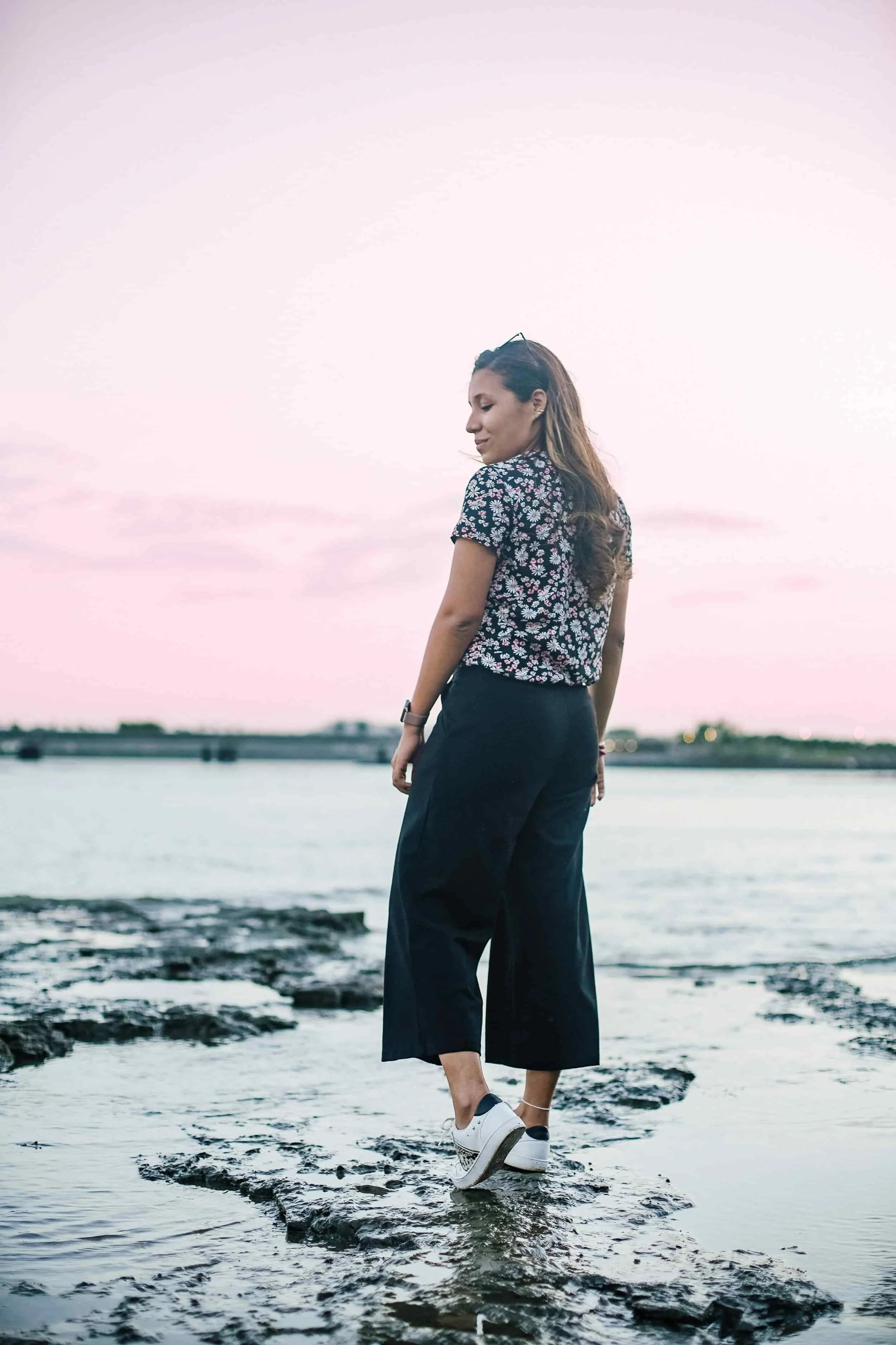 Woman smiling while walking on rocks a beach during sunset