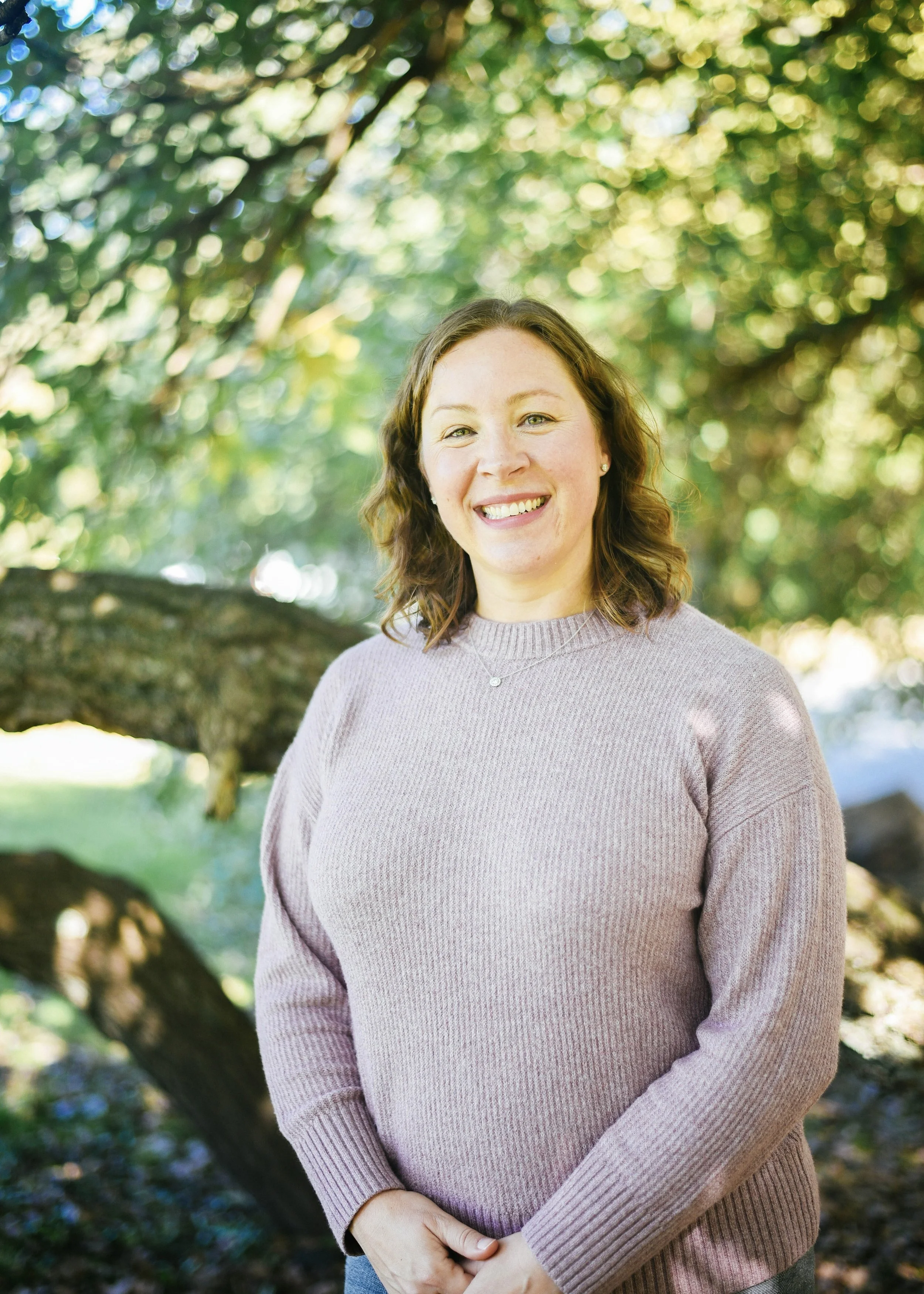 Emily Harlan smiling standing by green tree with low branches